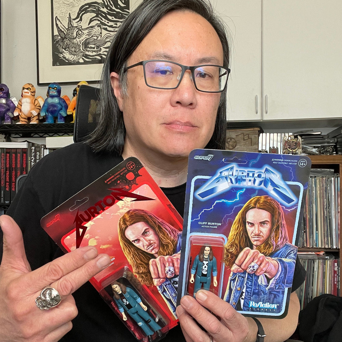Portrait of a person wearing glasses holding three colorful Super7 action figure packaging cards with comic style art.