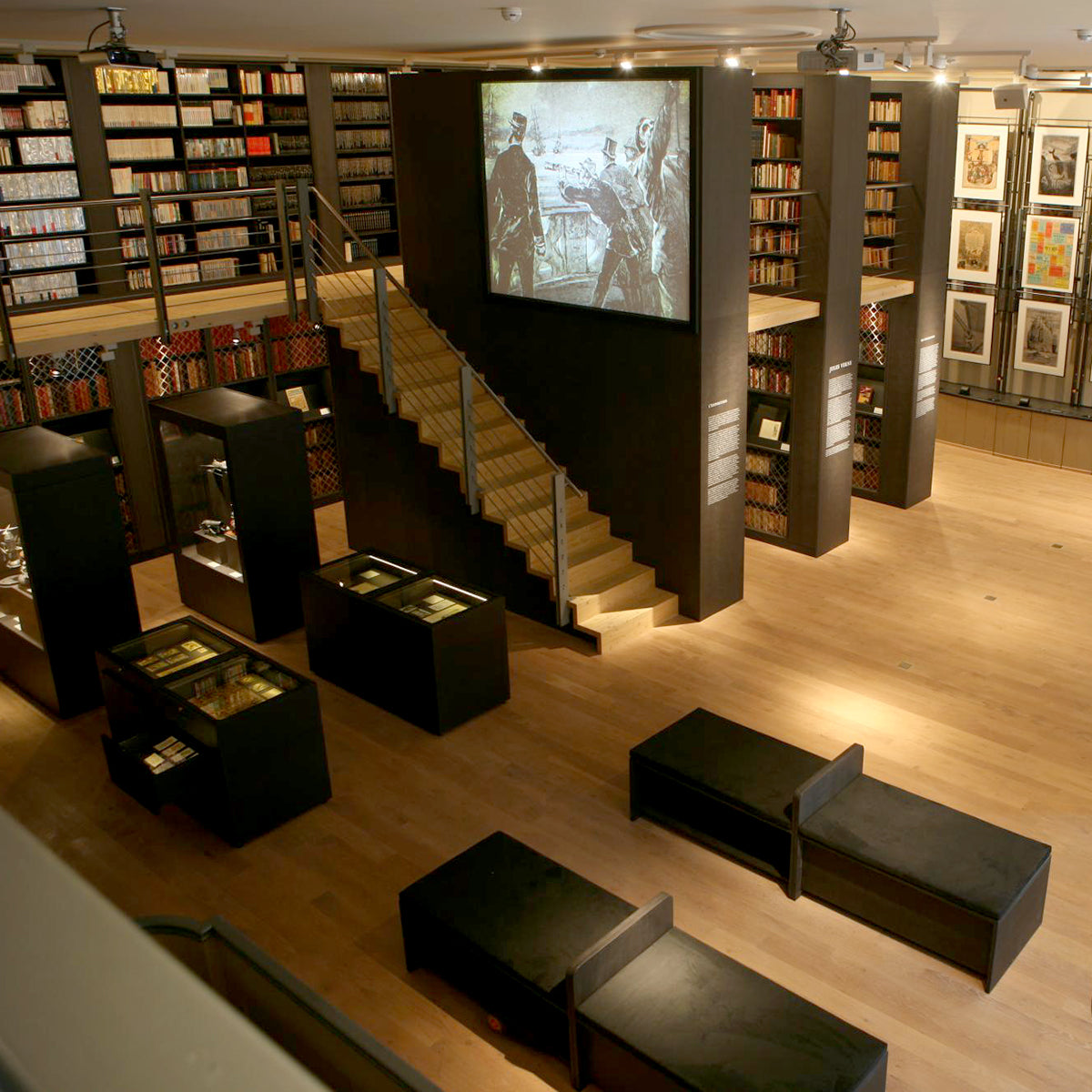 Exhibition space at Maison d’Ailleurs with tall bookshelves and a large central projection screen