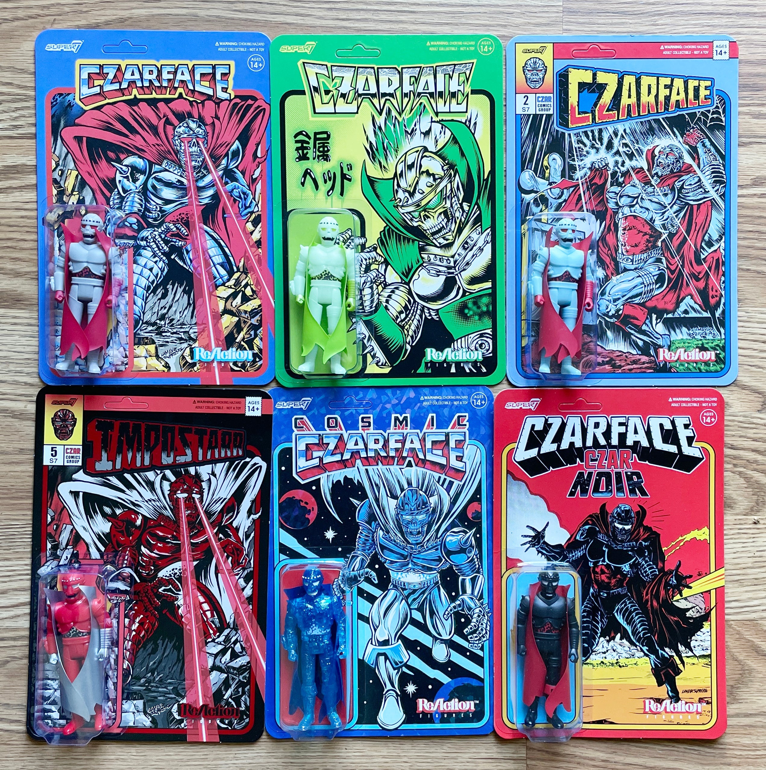 Three Czarface Super7 action figure cards spread on a wooden surface showing blue green and red artwork with figures in the blisters.