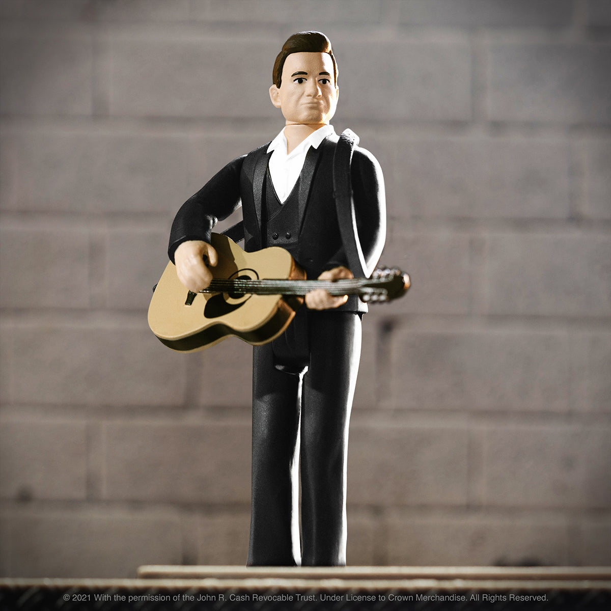 Johnny Cash action figure in a black suit strums a guitar against a gray brick backdrop.