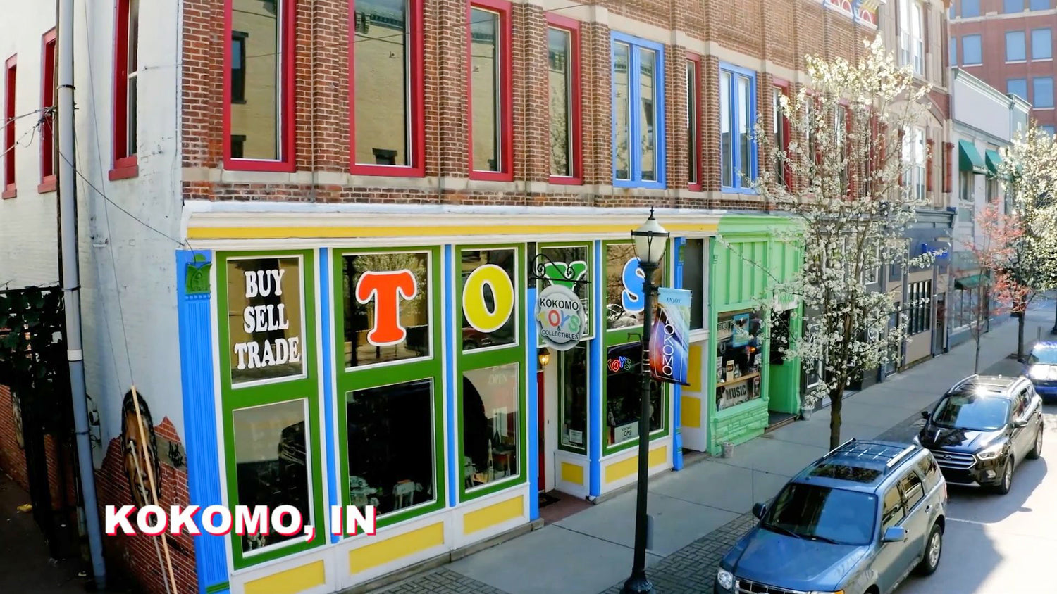 Colorful Kokomo Toys storefront on a sunny street with bright green and yellow trim and bold BUY SELL TRADE lettering in the windows