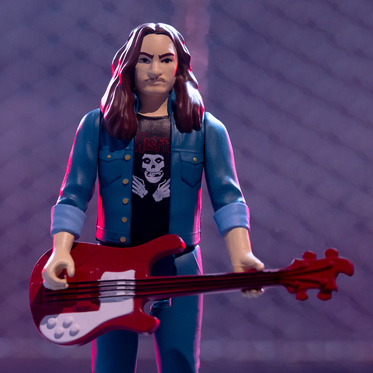 Cliff Burton ReAction figure with long hair wearing a blue denim jacket and black shirt, holding a red bass guitar.