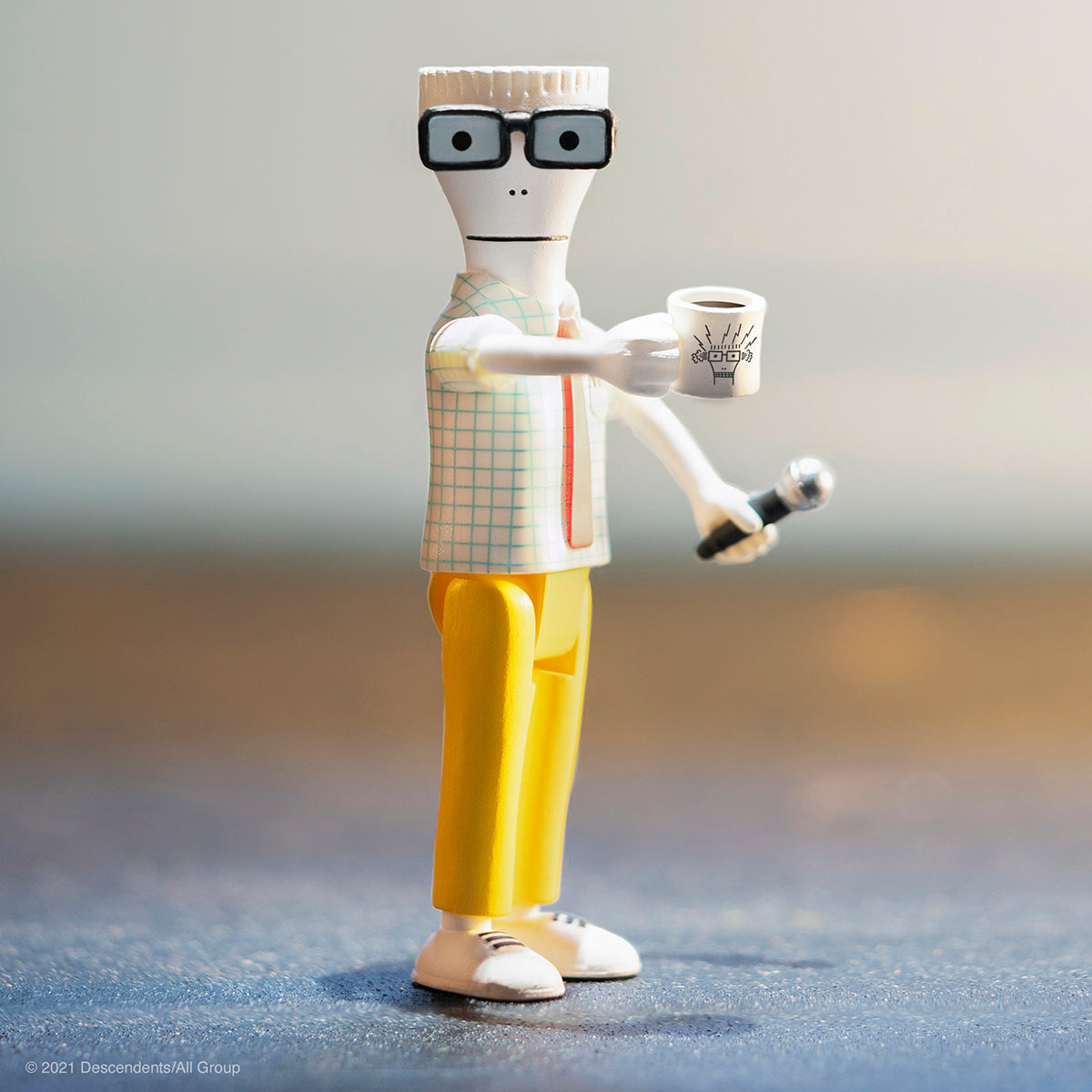 Plastic action figure with square glasses, checkered shirt and yellow pants holding a mug and a microphone