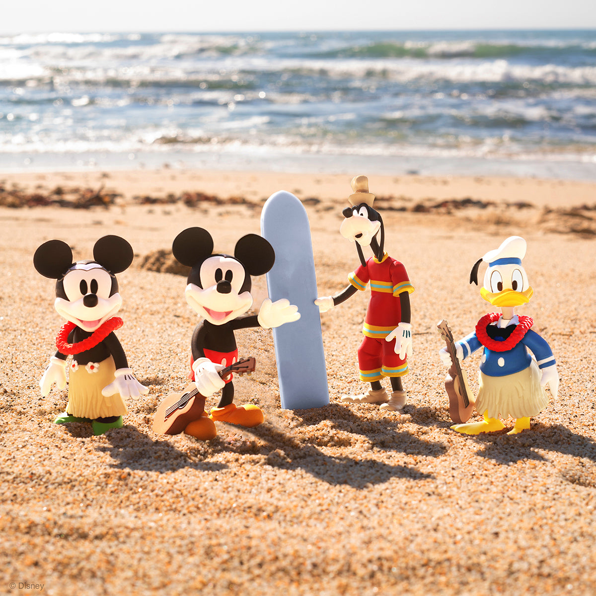 Mickey and Minnie Mouse with Goofy and Donald Duck figurines on a sunny Hawaiian beach beside a blue surfboard
