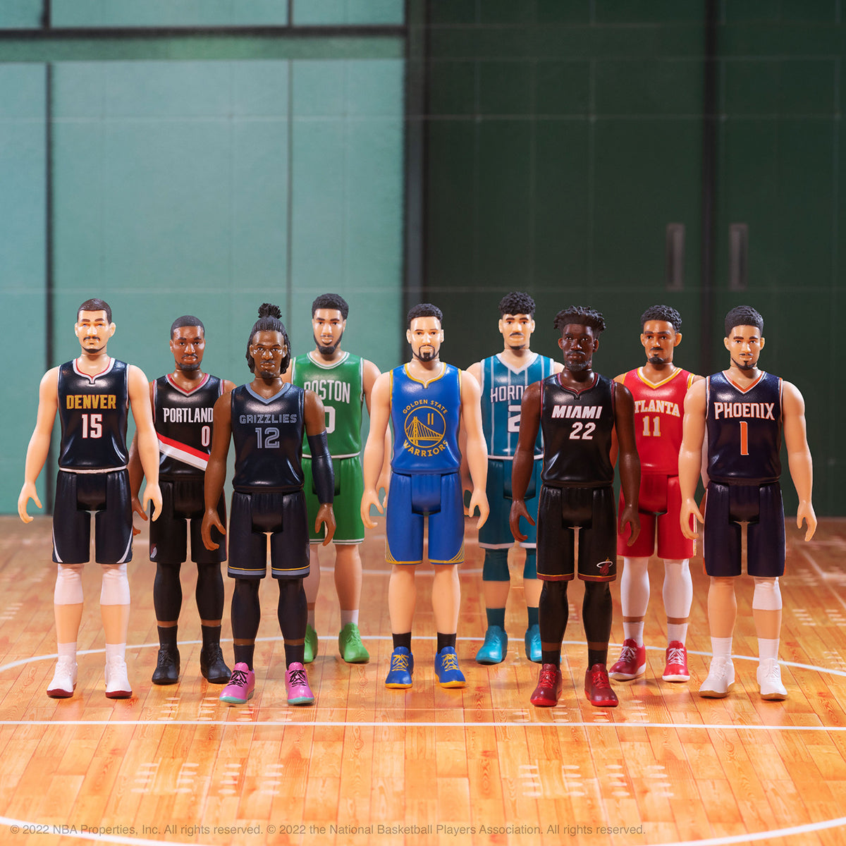 Line of NBA action figures wearing various team jerseys on a polished basketball court