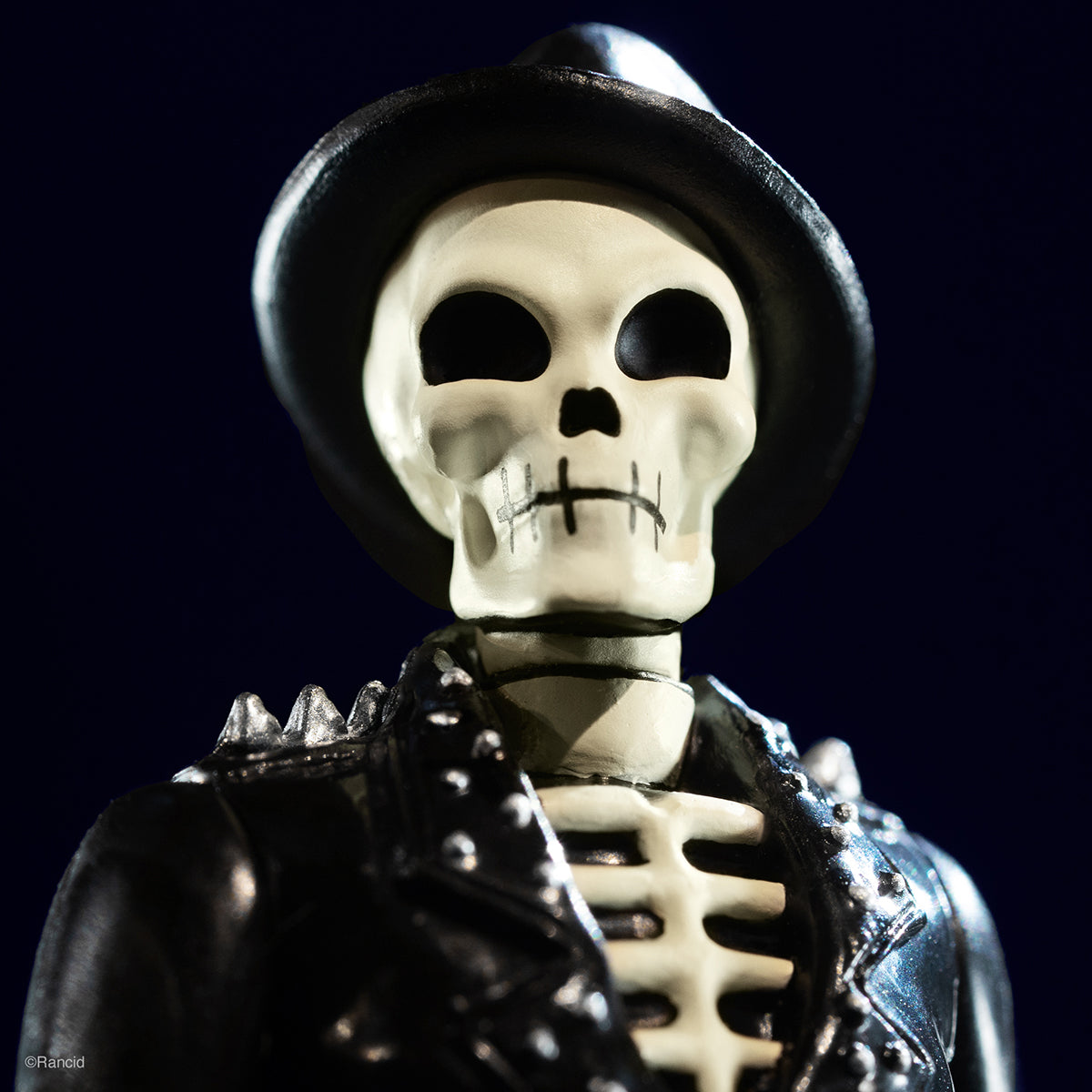 Skeleton figure in a black top hat and studded leather jacket against a dark background