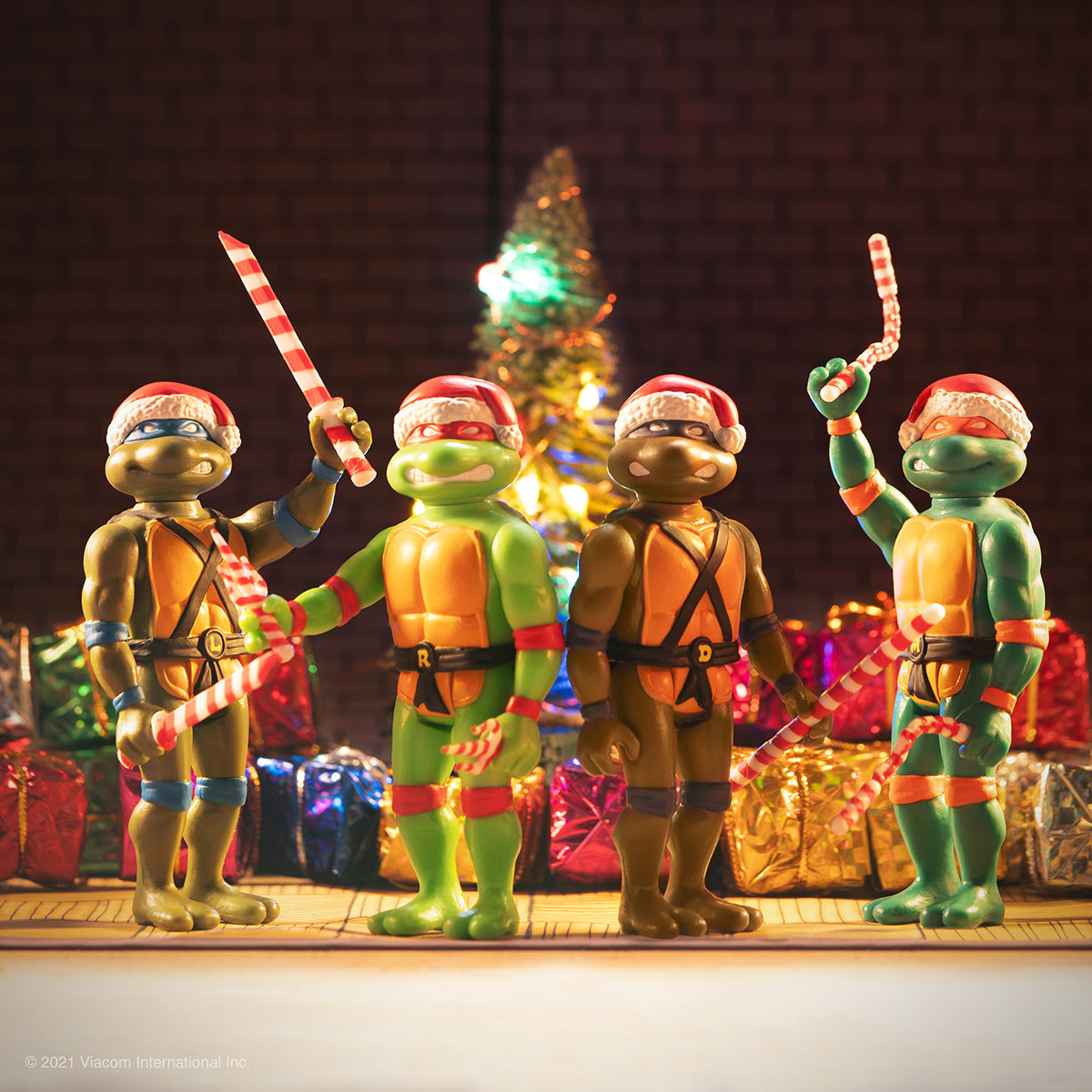 Teenage Mutant Ninja Turtles action figures in Santa hats with candy canes before a Christmas tree and wrapped gifts.