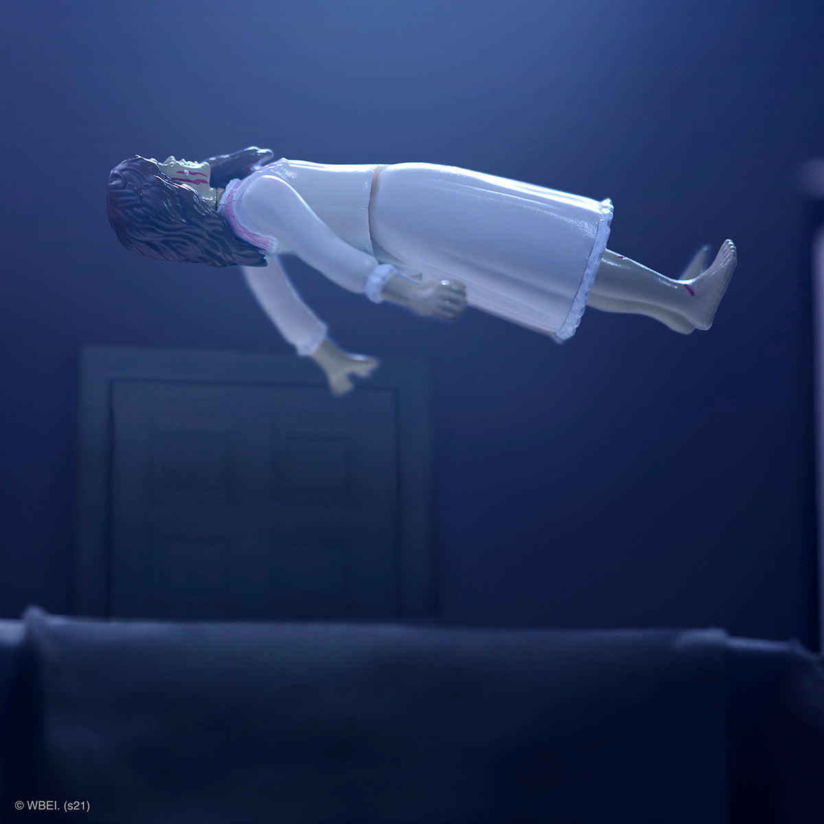 Regan MacNeil action figure floats in a white nightgown under blue lighting