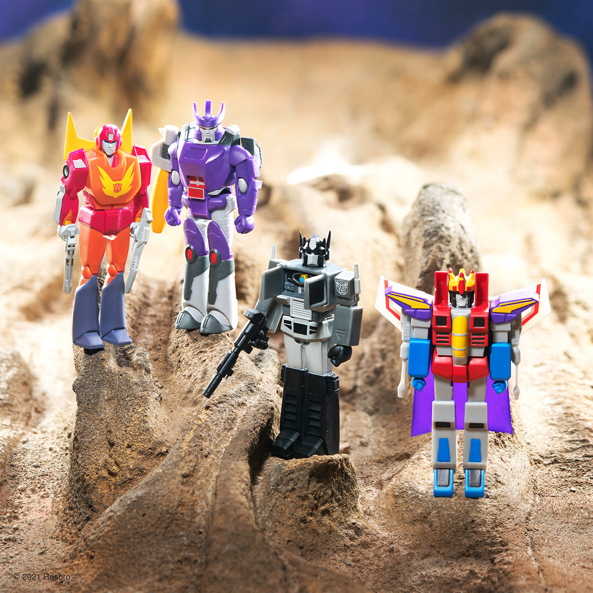 Group of Transformers action figures posed on a rocky desert diorama celebrating The Movie 35th anniversary.