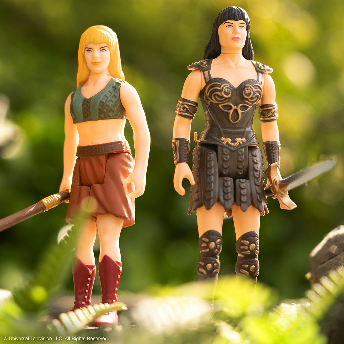 Xena the Warrior Princess and a dark armored warrior action figure stand outdoors with weapons.