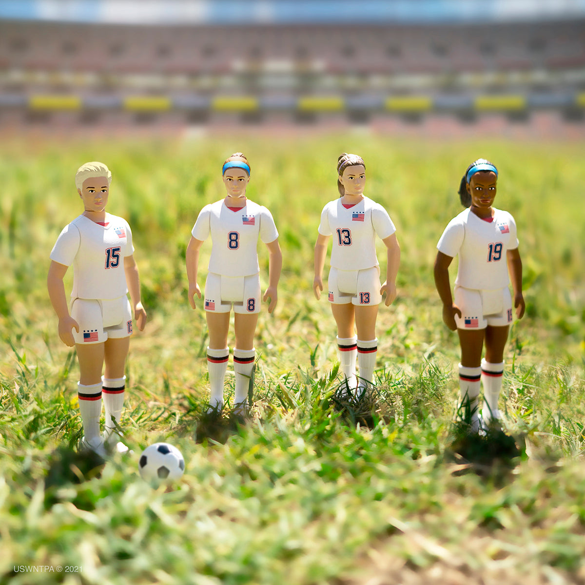 USWNT Supersports four player action figure lineup in white uniforms on a grassy field with a soccer ball.