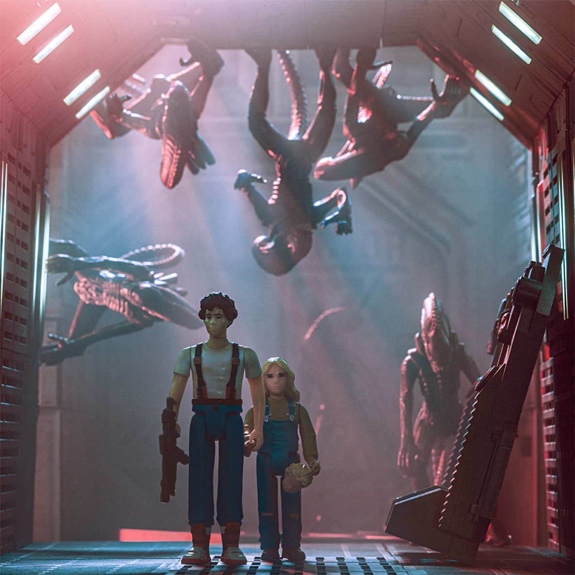 Two adults and a young girl action figures stand in a neon-lit sci fi display with looming alien creatures overhead.