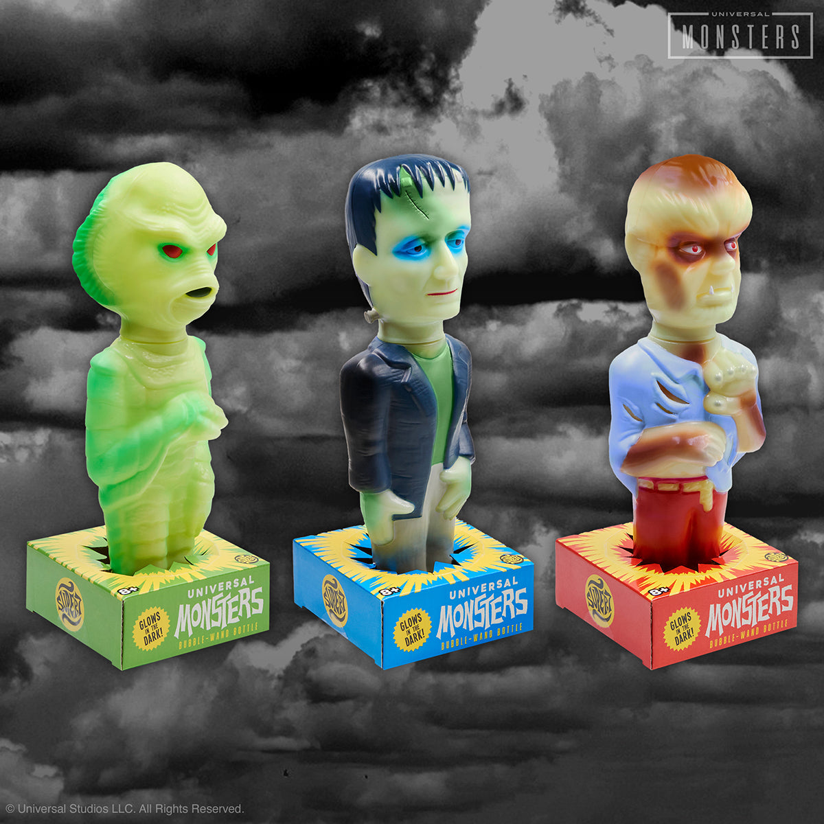 Three neon Universal Monsters bubble wand figures on their branded boxes against a cloudy backdrop