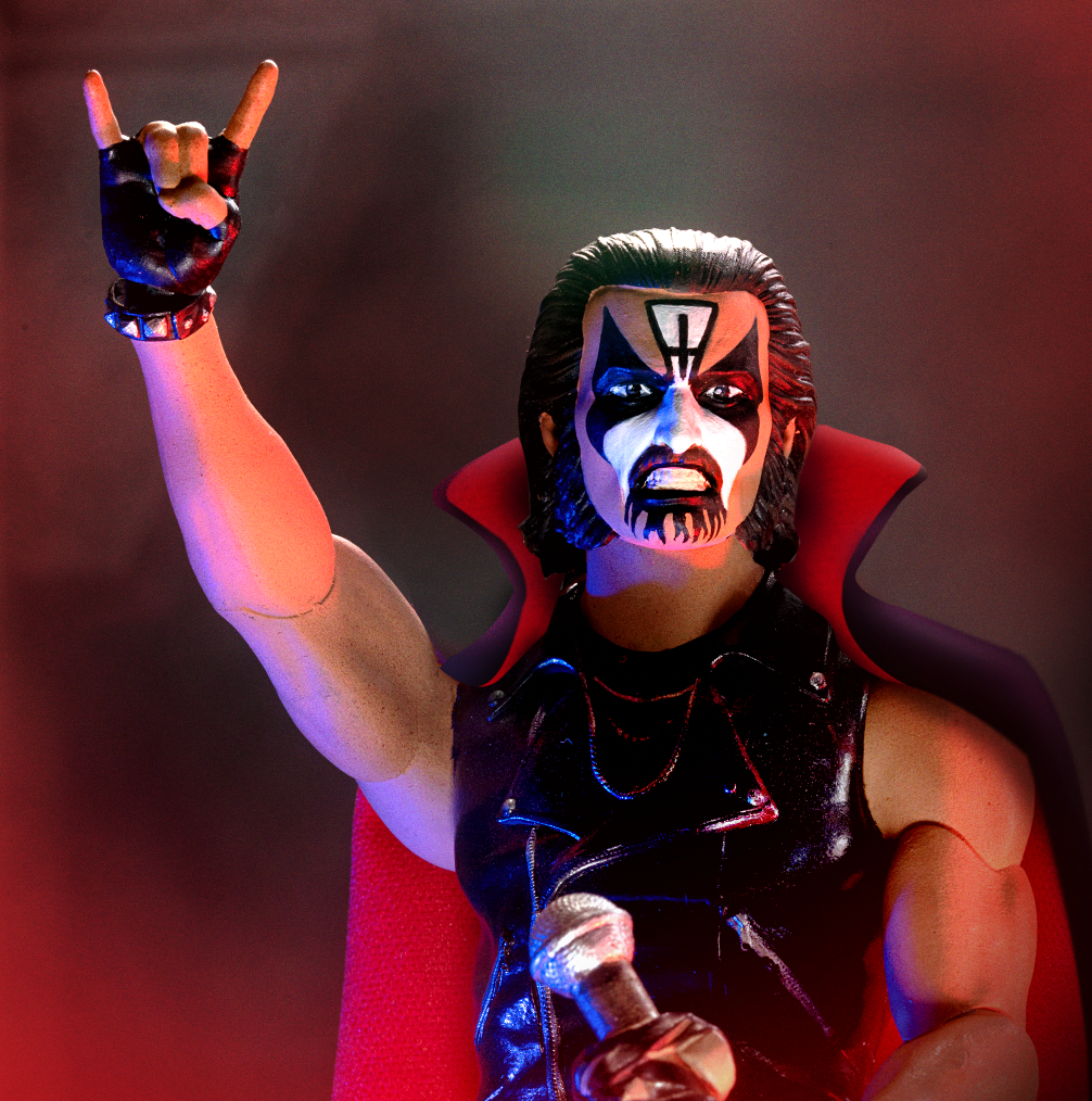 King Diamond ULTIMATES! action figure with painted face and black leather, raising horns against red stage light.
