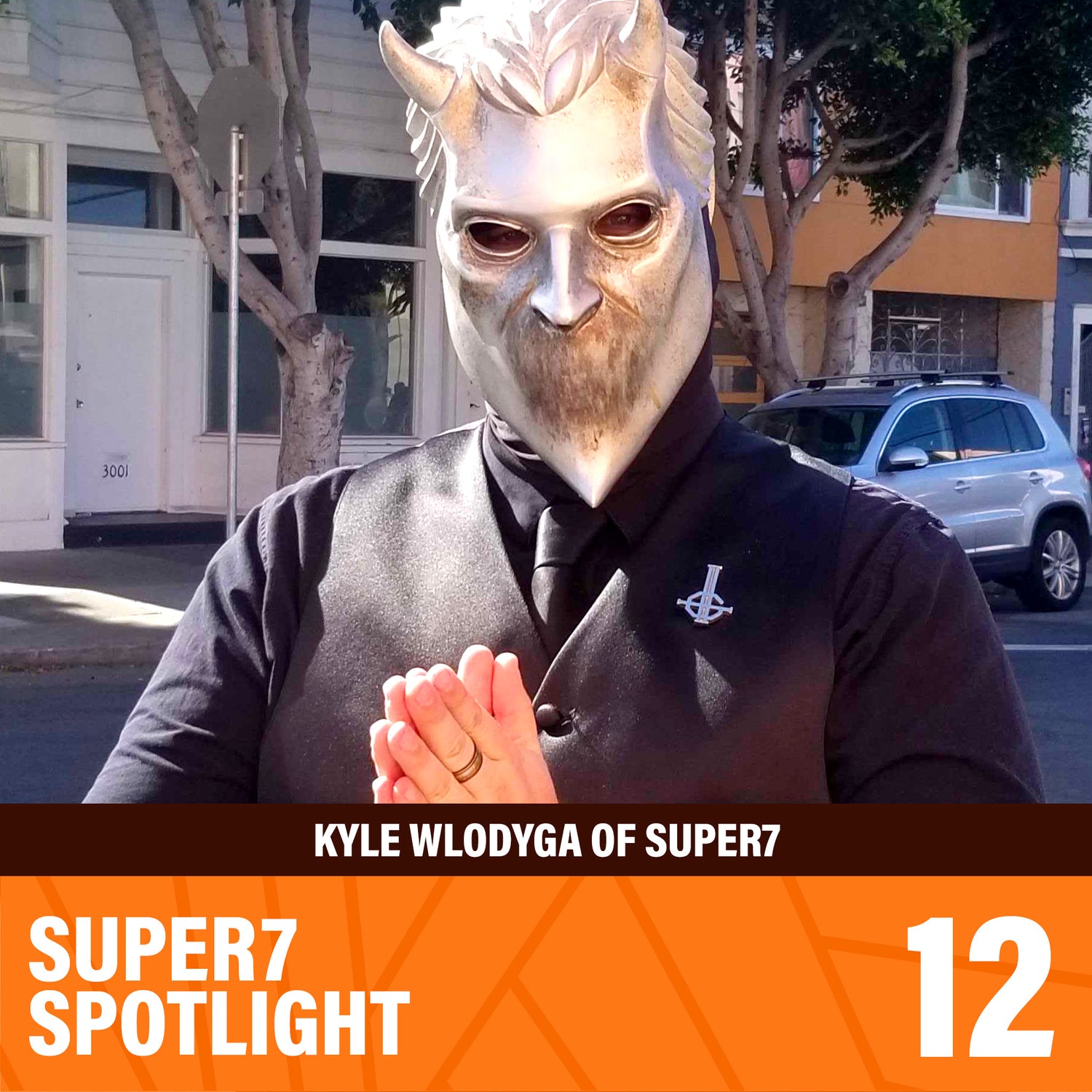 Individual in a large metallic horned mask outdoors with a city street background.