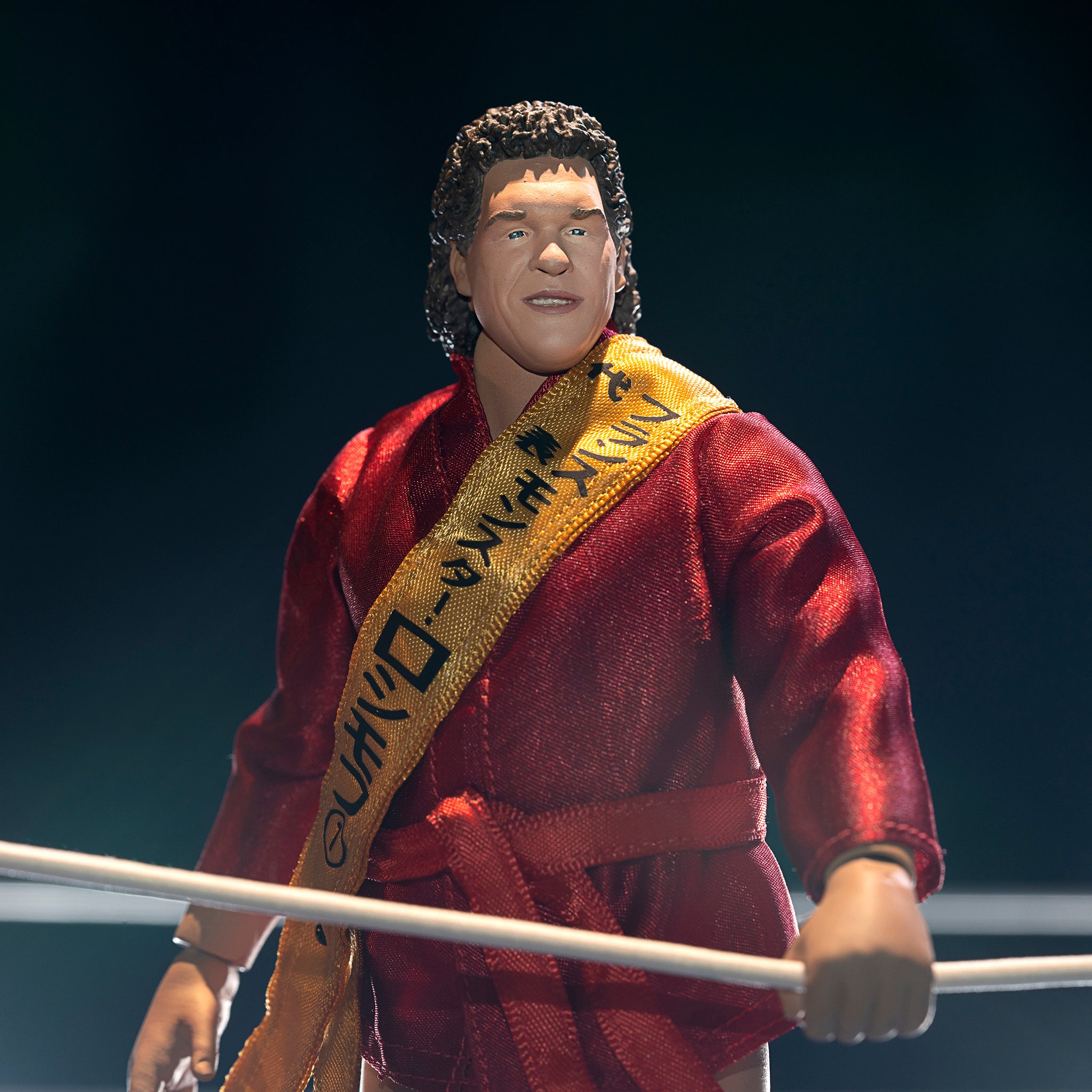 Action figure of a wrestler in a red robe with a gold sash standing by a ring rope