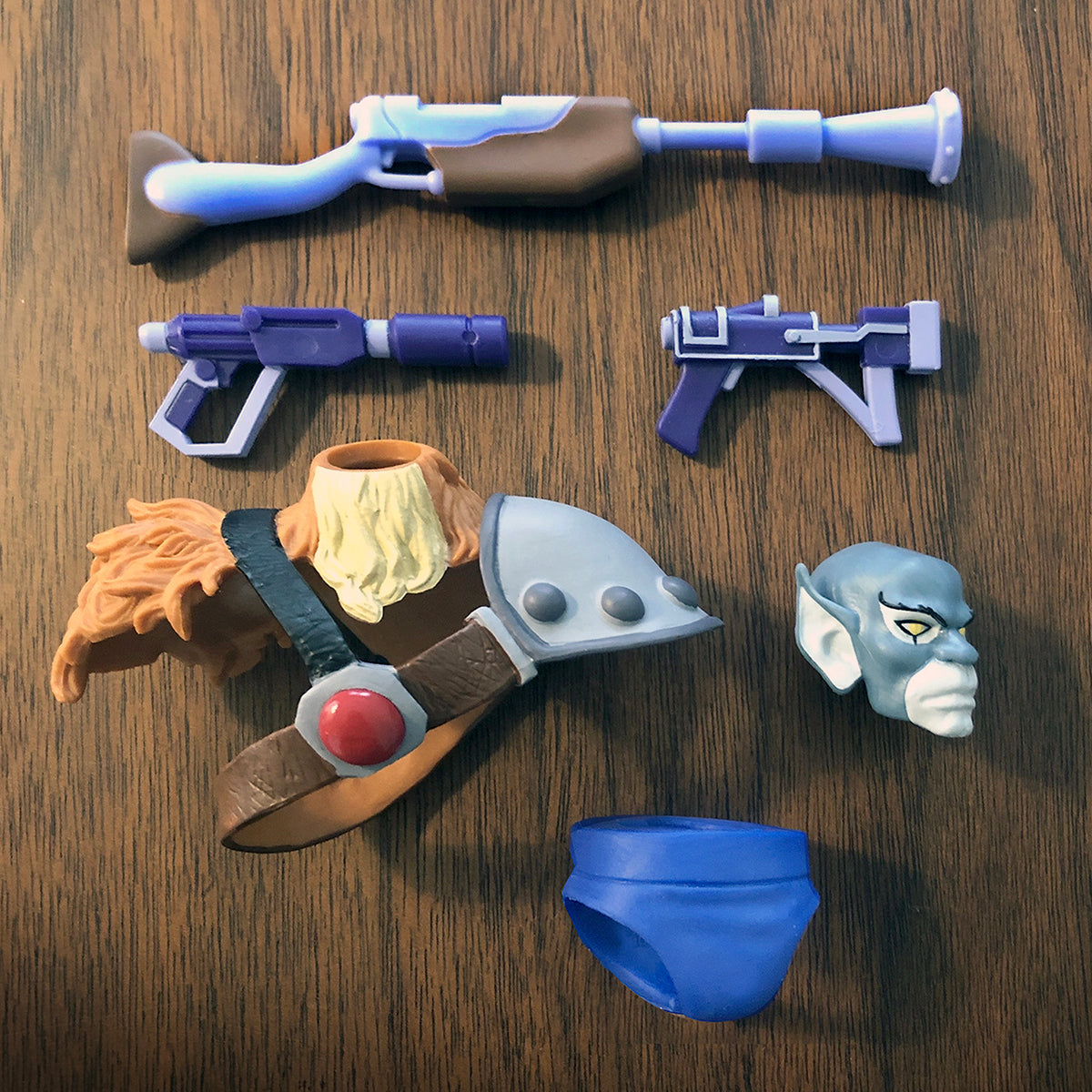 Assorted replacement parts booster pack for ThunderCats ULTIMATES laid out on a wood surface with weapons and armor