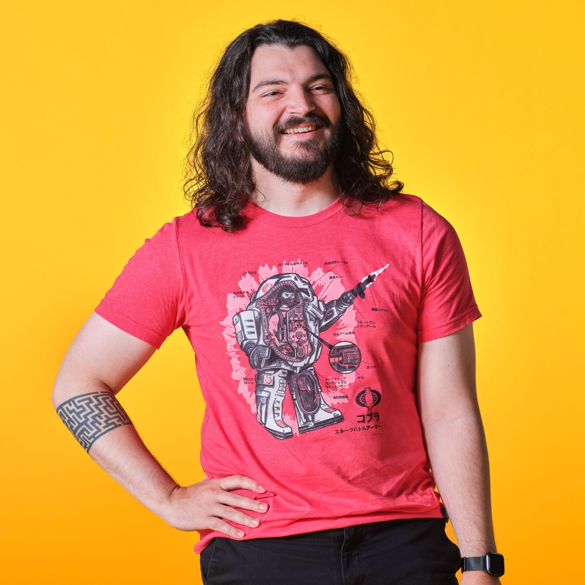 Man with long hair and beard wearing a red Last Chance Apparel T shirt smiles against a bright yellow backdrop