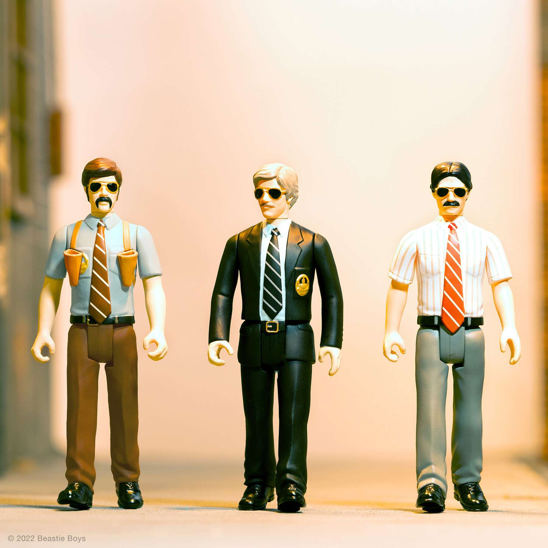 Three vintage hip hop action figures wearing sunglasses and ties stand in a row.