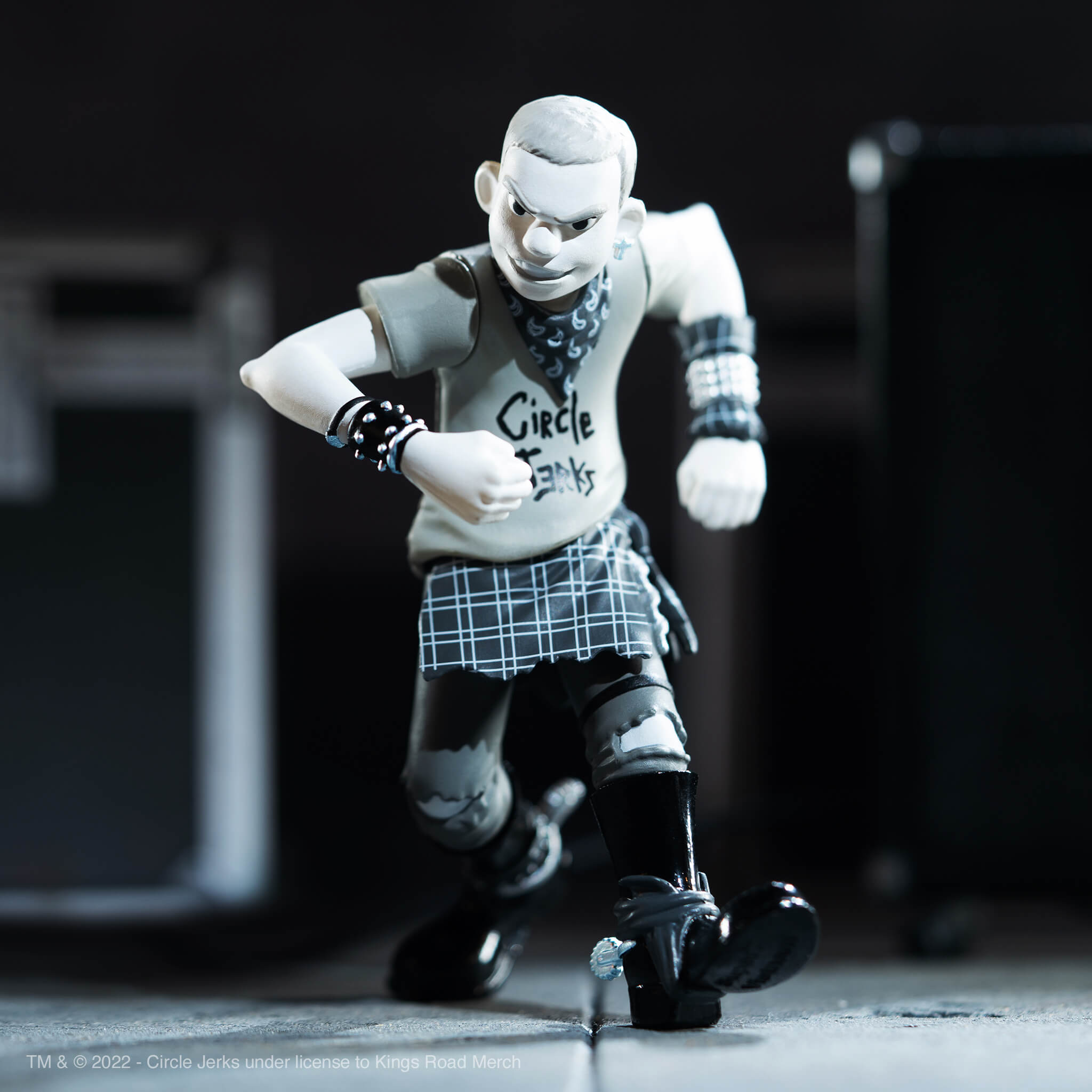 Close up of a pale white action figure in a dynamic pose wearing a scarf and bracelets against a dark backdrop