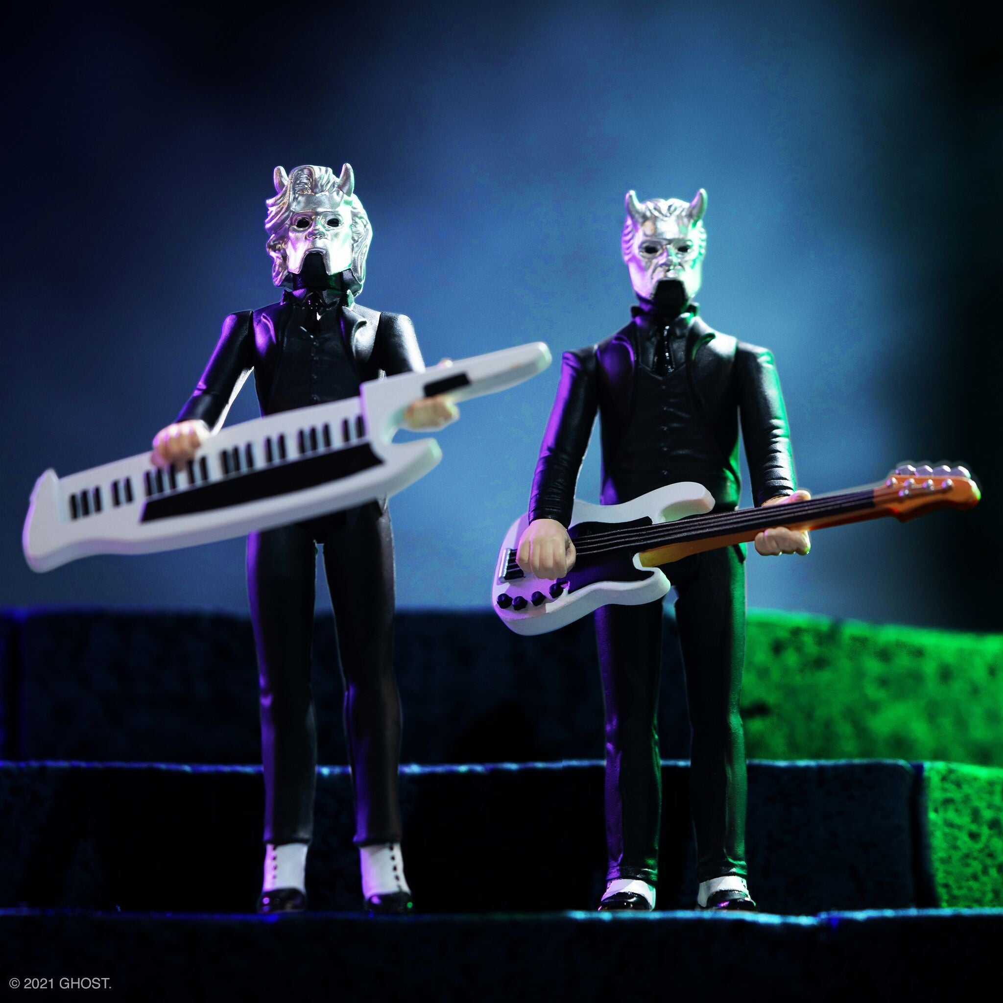 Two humanoid musicians in black suits and metallic masks play a keyboard and a guitar on stage