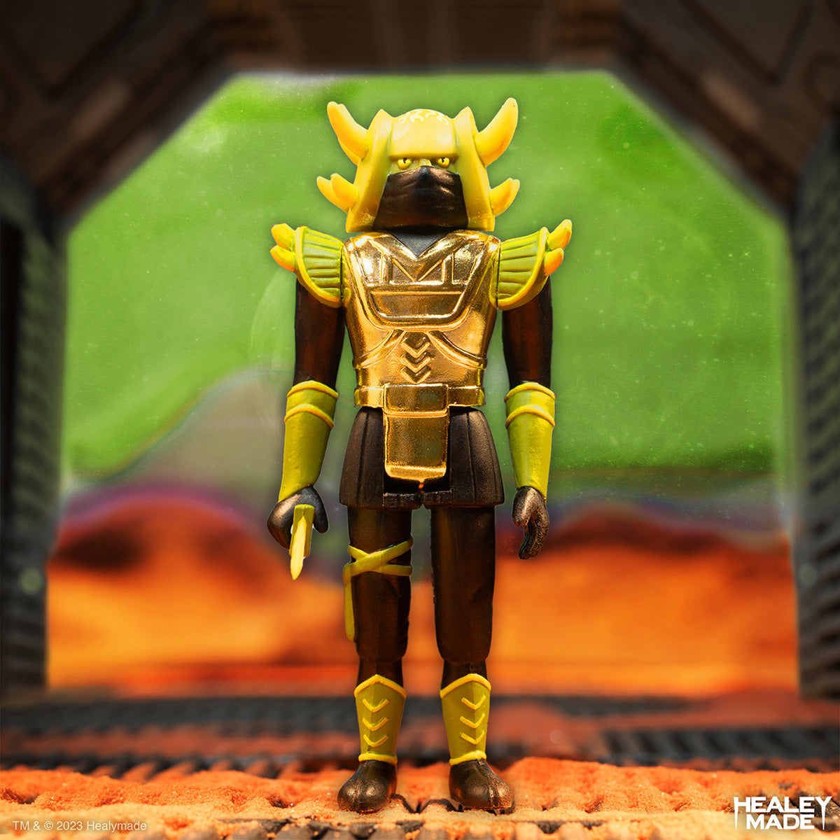 Healeymade gold armored action figure stands in a sci fi diorama with orange ground and a green backdrop.