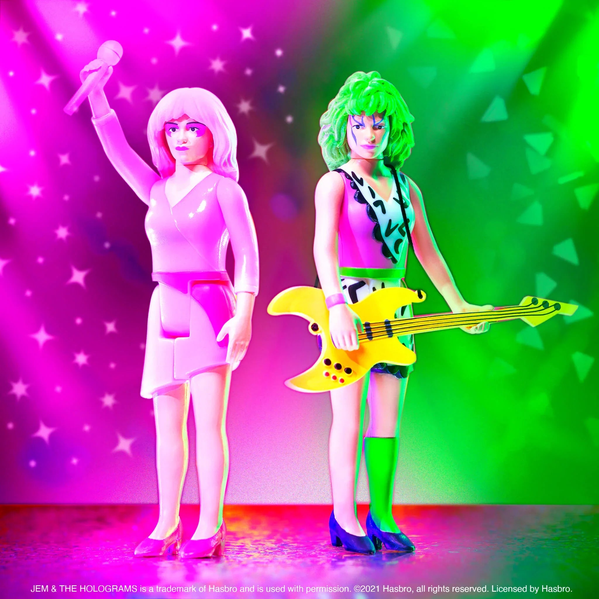 Jem and the Holograms action figures posed on a rocky stage with a vivid rainbow backdrop