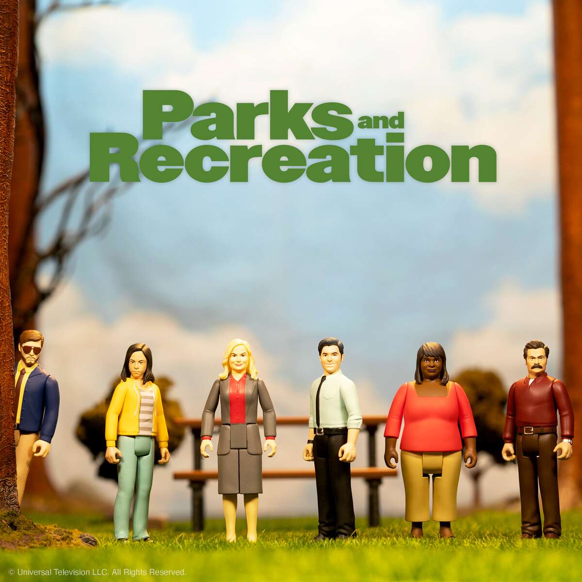 Six diverse action figures stand on grass beneath a Parks and Recreation backdrop