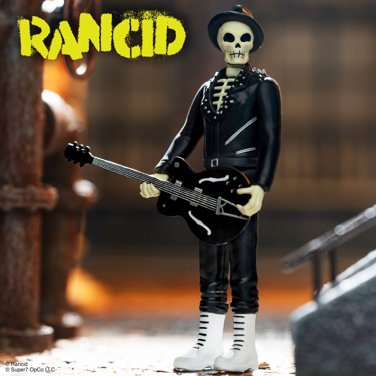Skeleton guitarist figurine from The Bones Collection wearing a black leather jacket and white boots with a RANCID logo in the upper left