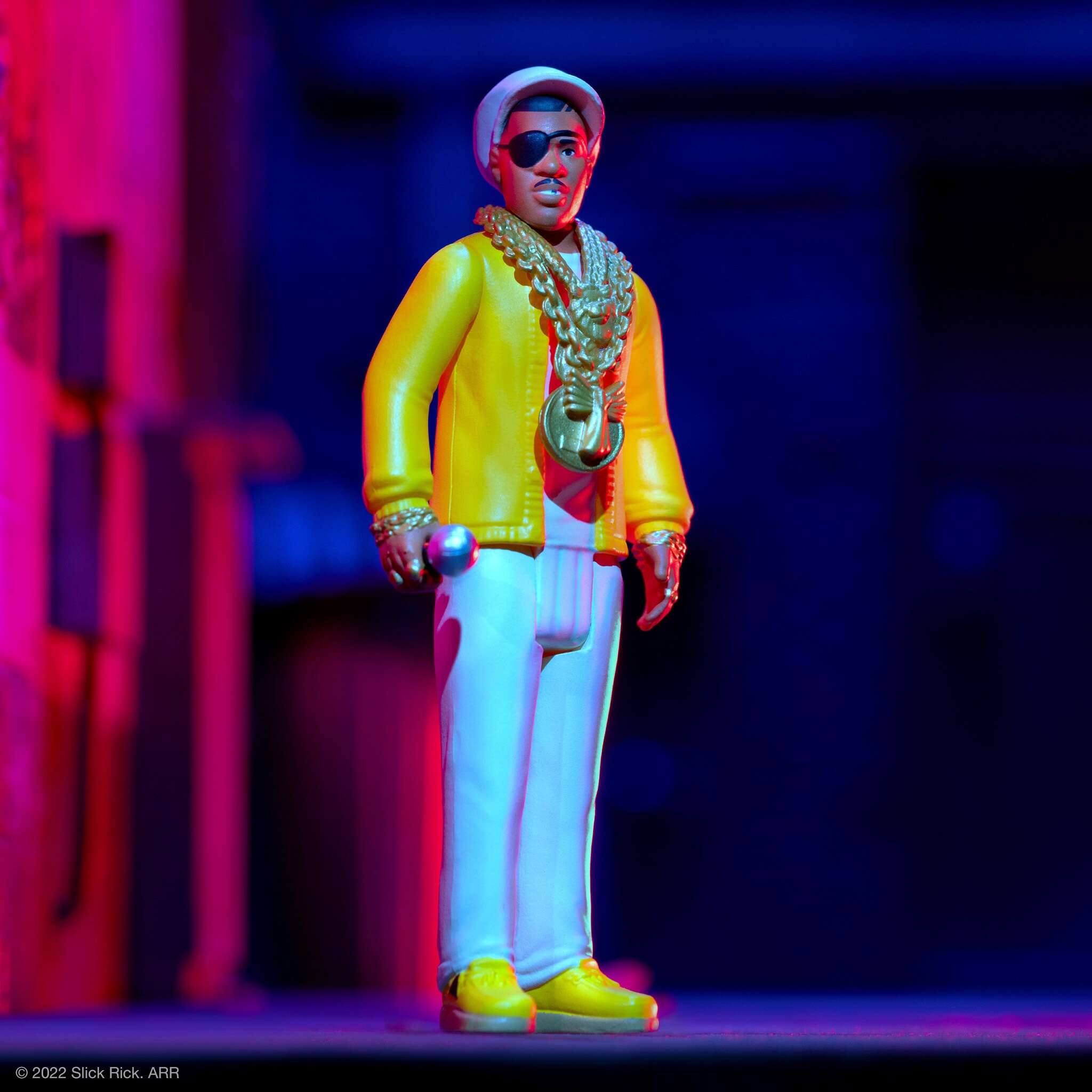 Slick Rick action figure in a bright yellow jacket with an oversized gold chain and an eye patch