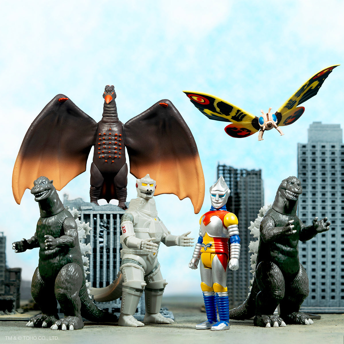 Group of monster action figures in a miniature city scene, including a winged red dragon and gray kaiju.