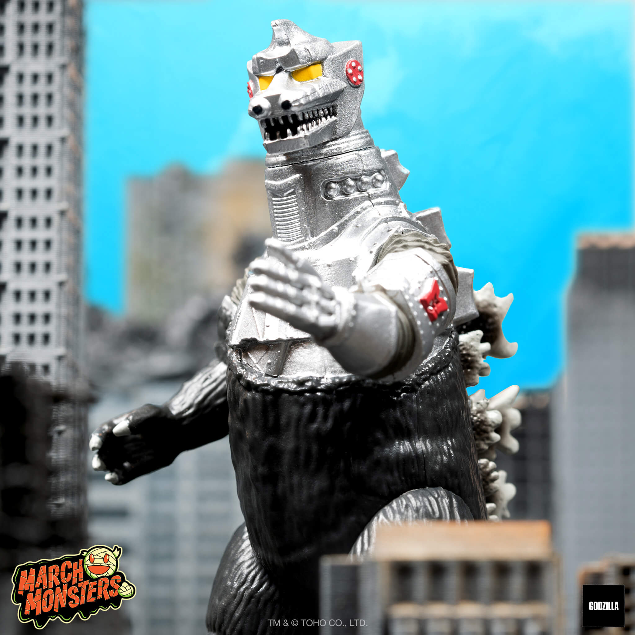 Silver Godzilla style monster figure in a city setting with March Monsters sticker