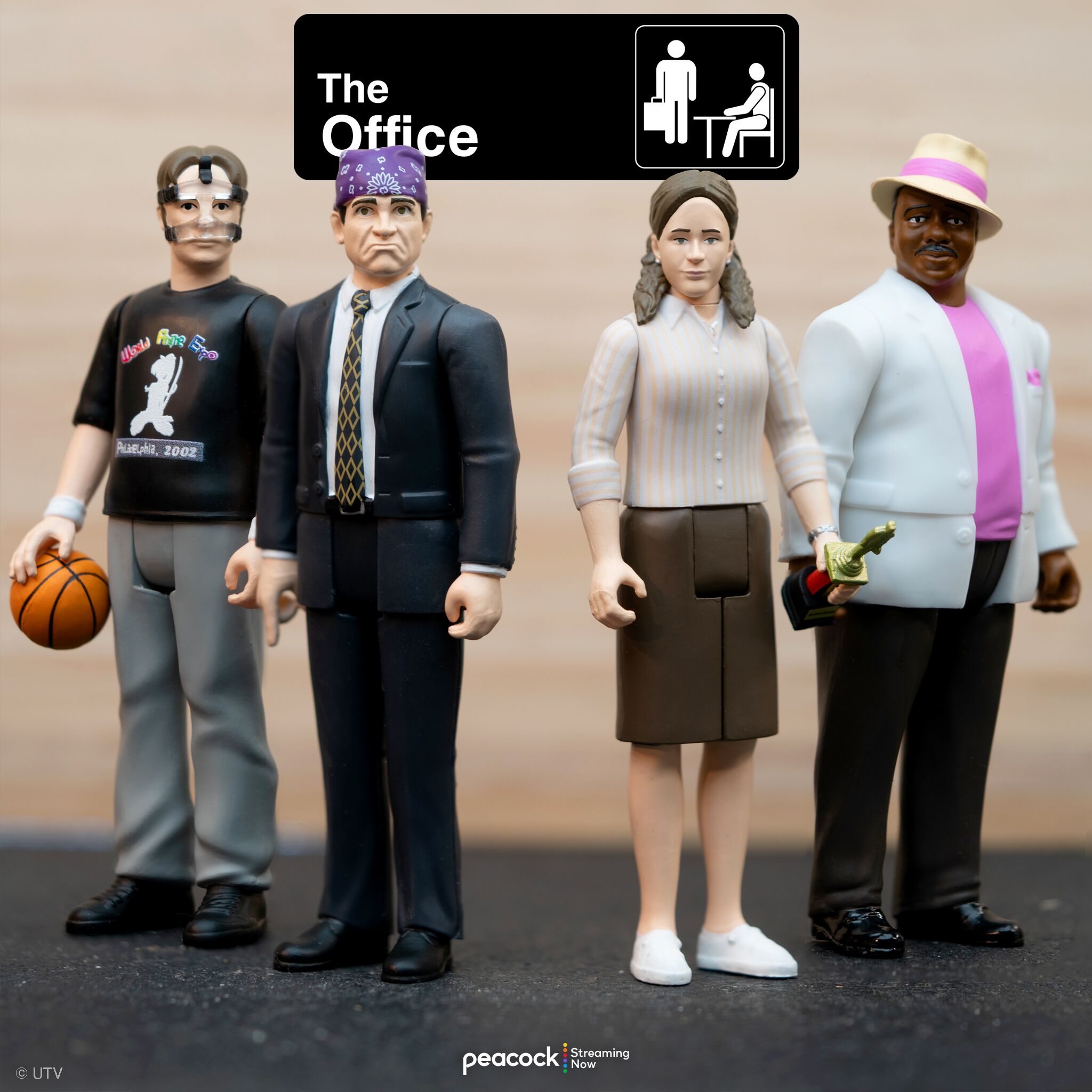 Group of four retro style action figures on a surface with a large The Office sign in the background.