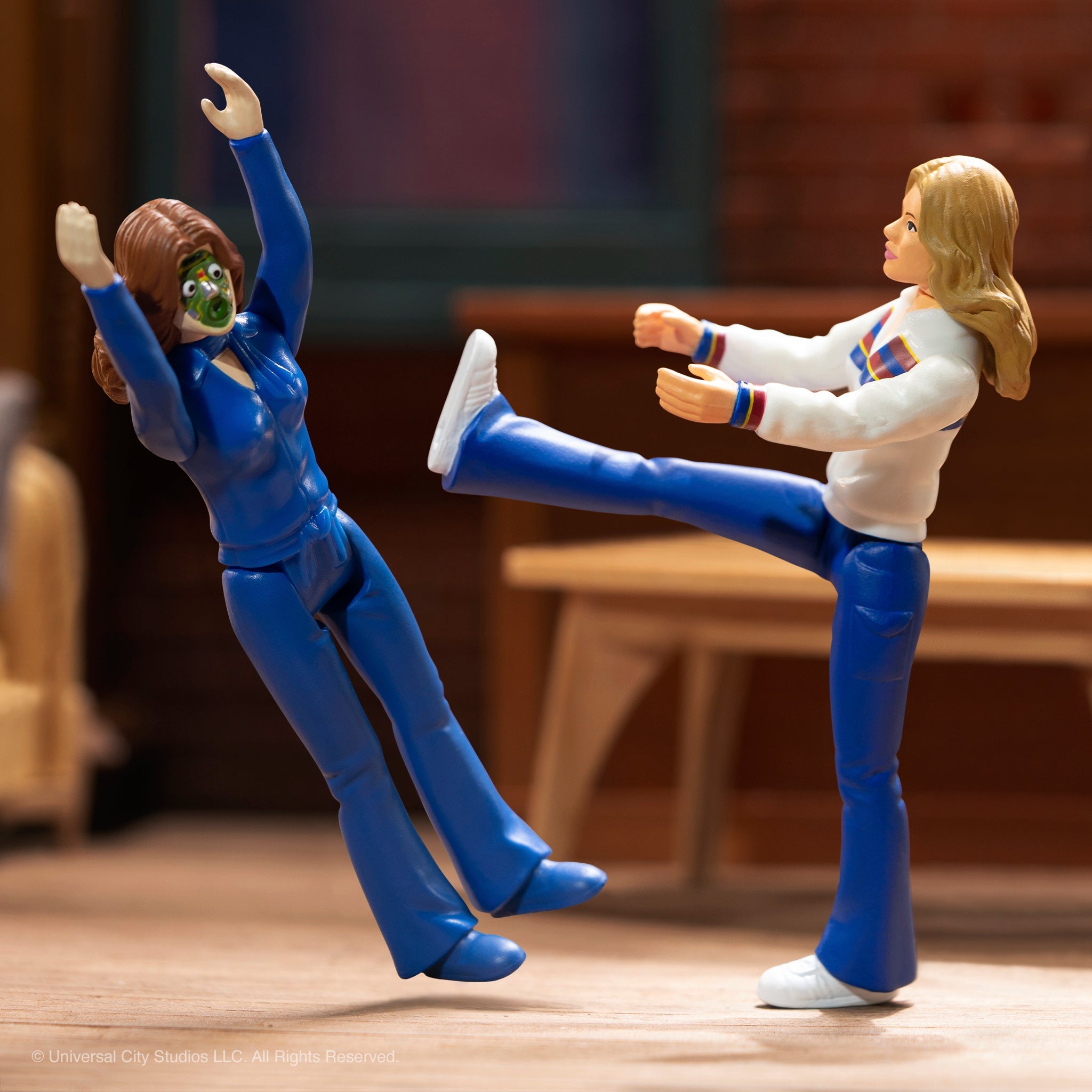 Two action figures mid kick fight scene, green masked villain in blue suit battling a blonde heroine in white jacket.