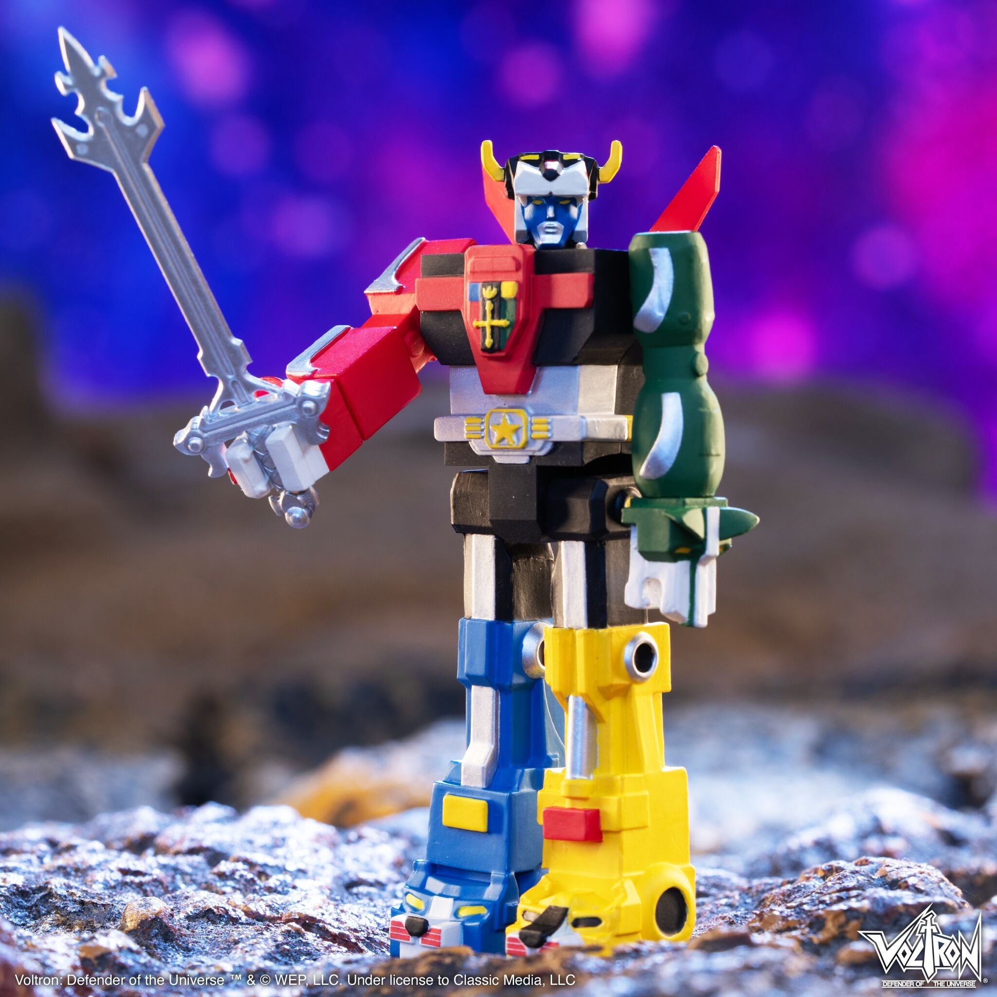 Voltron Defender of the Universe toy figure with a silver sword on rocky ground against a purple blue background.