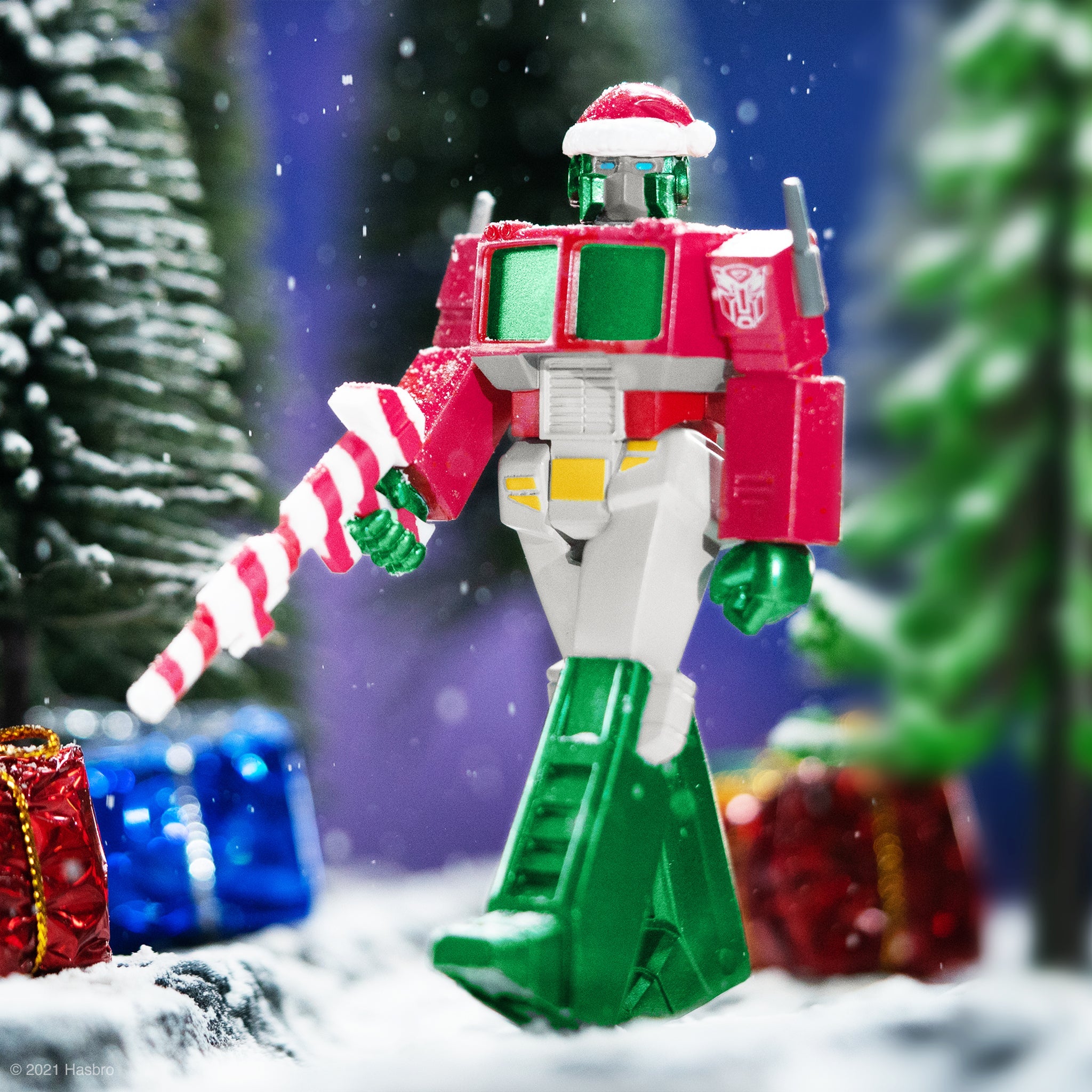 Red and green Transformer style robot wearing a Santa hat stands in a snowy holiday scene with blurred trees in the background