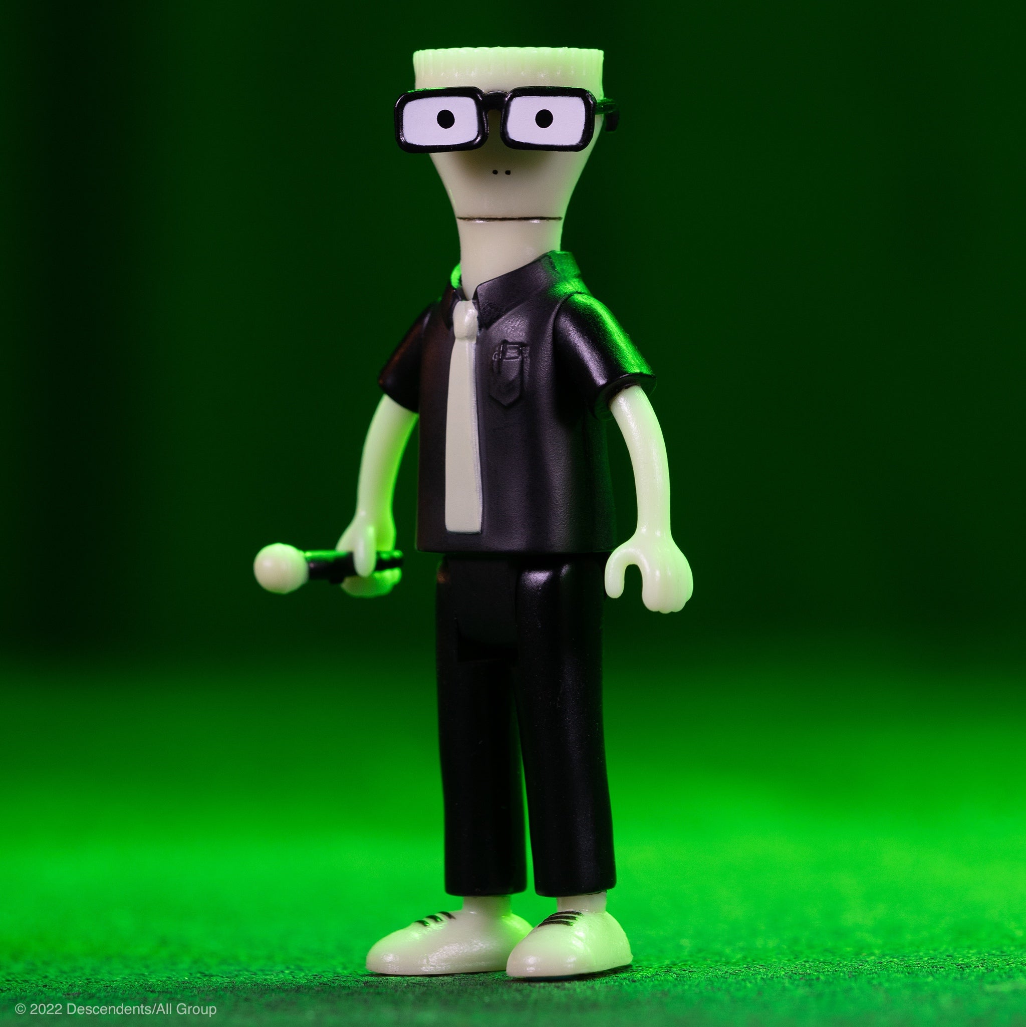 Descendents figure close-up showing a pale head with black framed glasses and a dark jacket against a green background