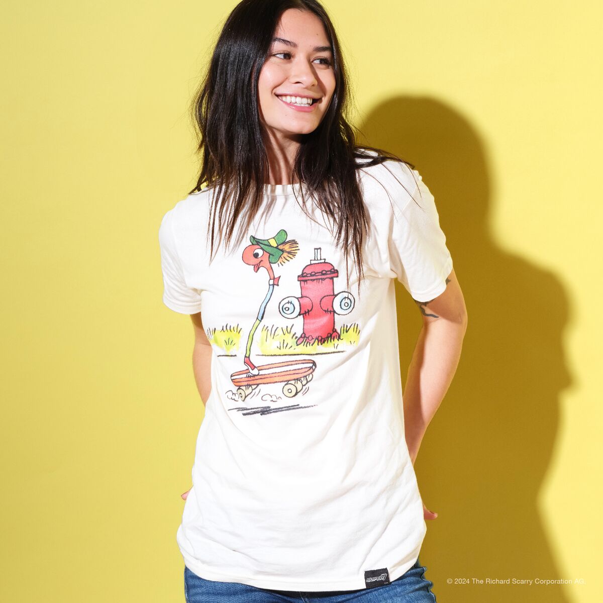 Smiling woman wearing a white graphic T shirt against a bright yellow backdrop.