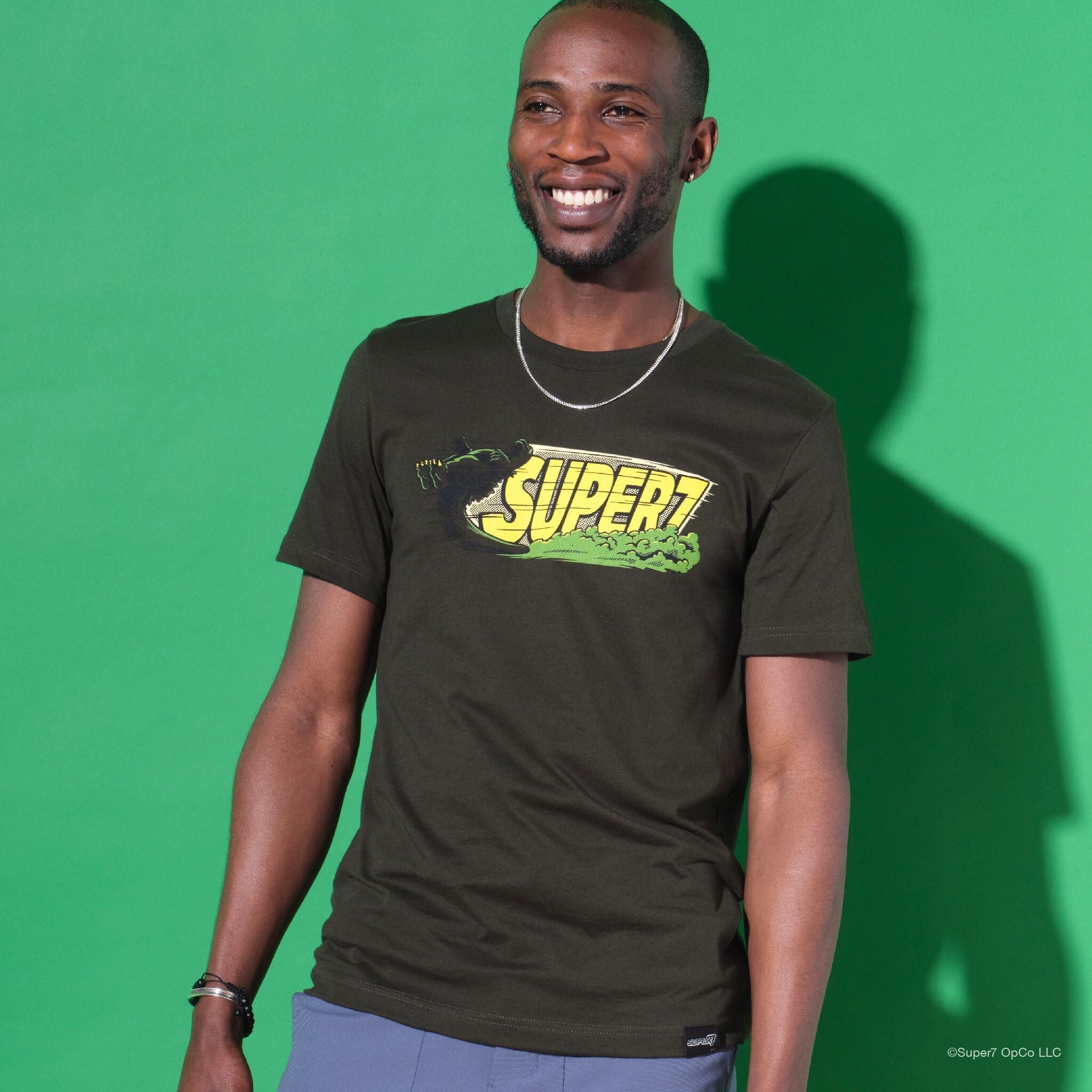 Smiling man wearing a black graphic t shirt and silver chain against a bright green backdrop.