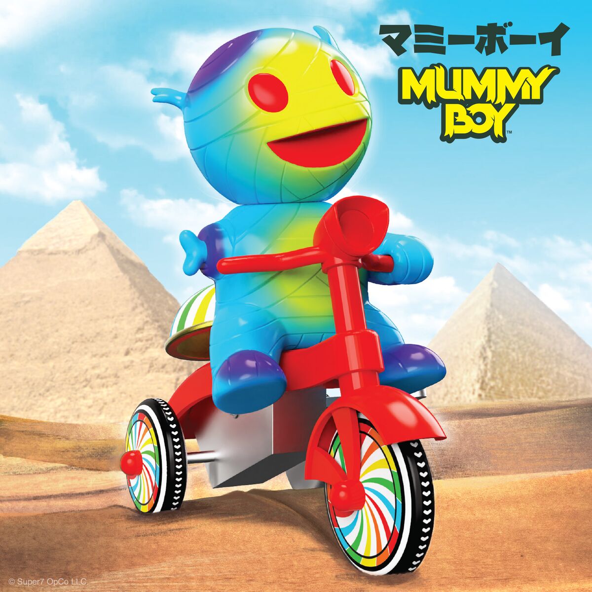 Rainbow colored mummy riding a red tricycle with rainbow wheels in a desert with pyramids and blue sky