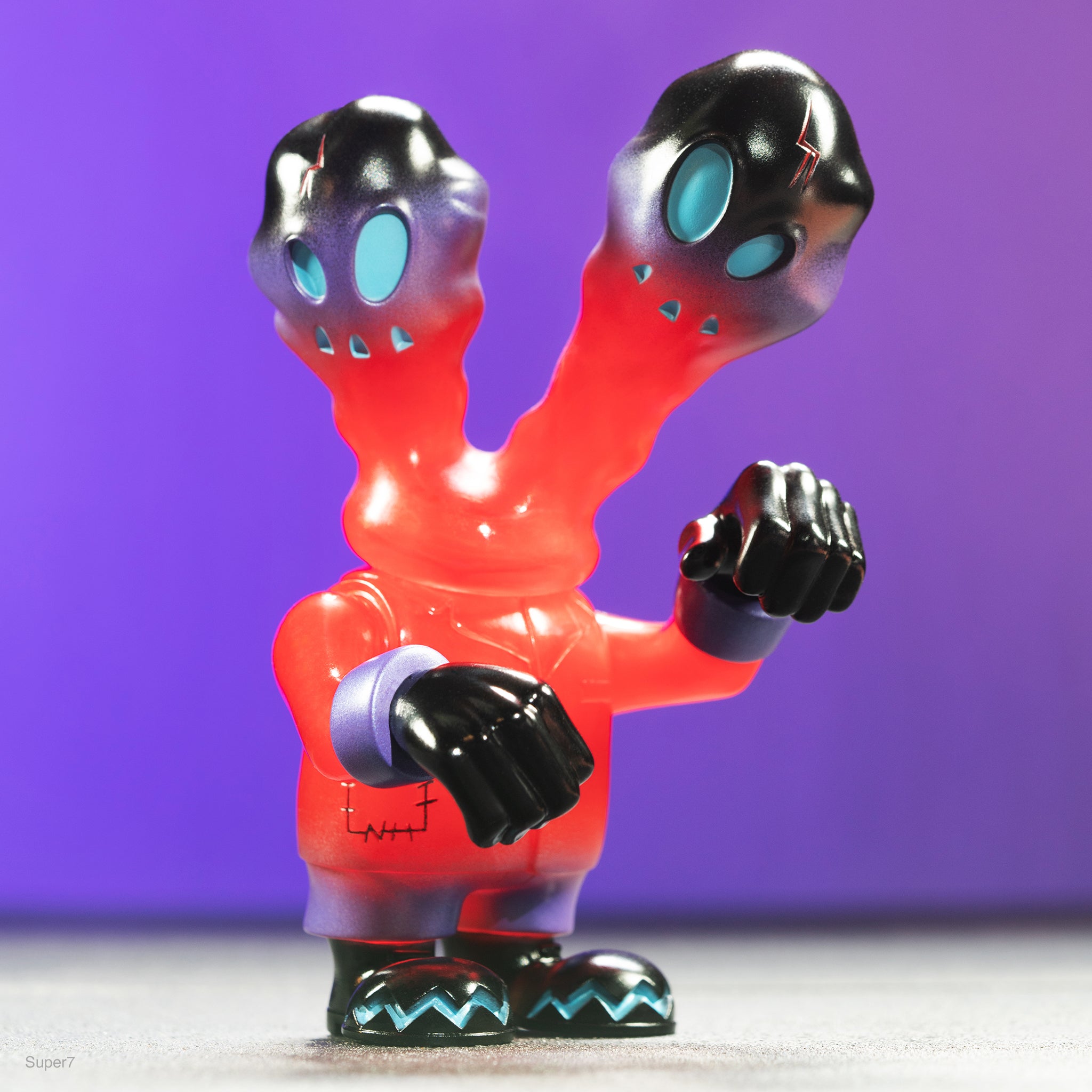 Two red glossy designer toy figures with black heads and teal oval eyes against a purple background.