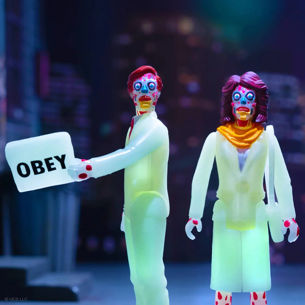 Two neon skeleton action figures from ReAction Figures stand side by side, the left one holding a sign that reads OBEY.