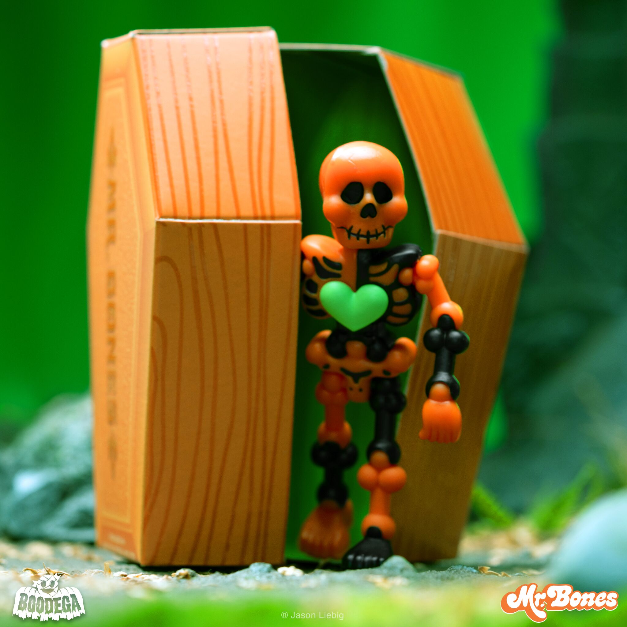 Orange and black skeleton toy with a green heart, standing in an open coffin