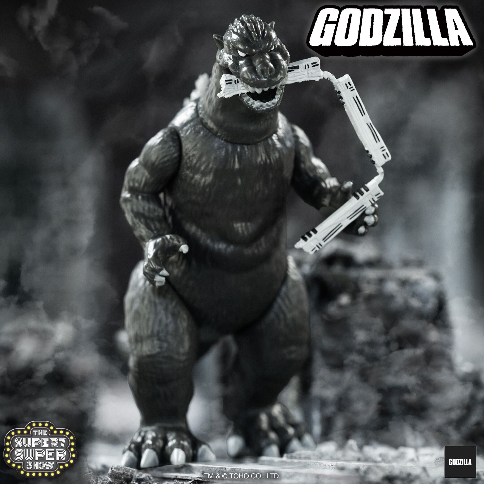 Grayscale close up of Godzilla 1954 Train Biter gripping a white rail against a smoky backdrop