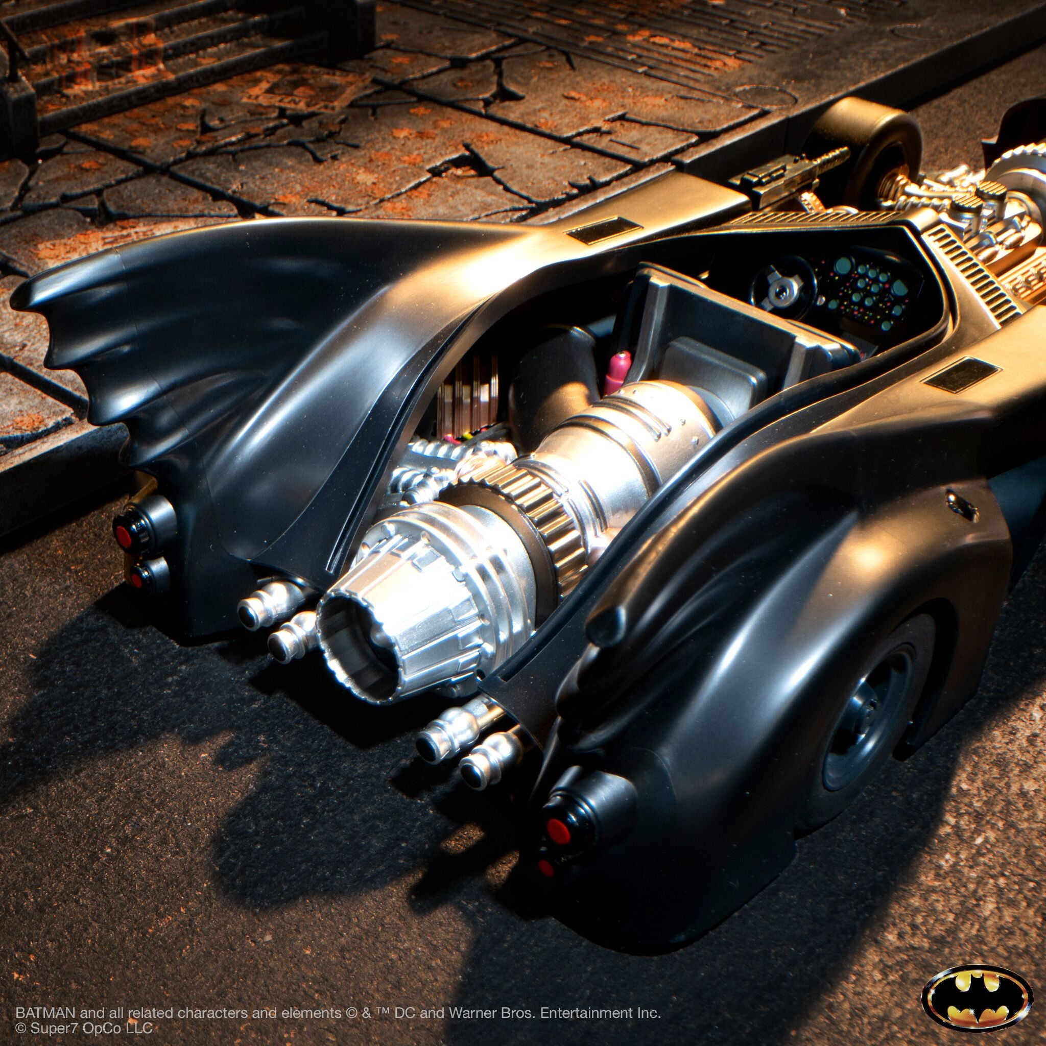 Close up of Batmobile front with exposed machinery on cracked pavement and Batman logo visible