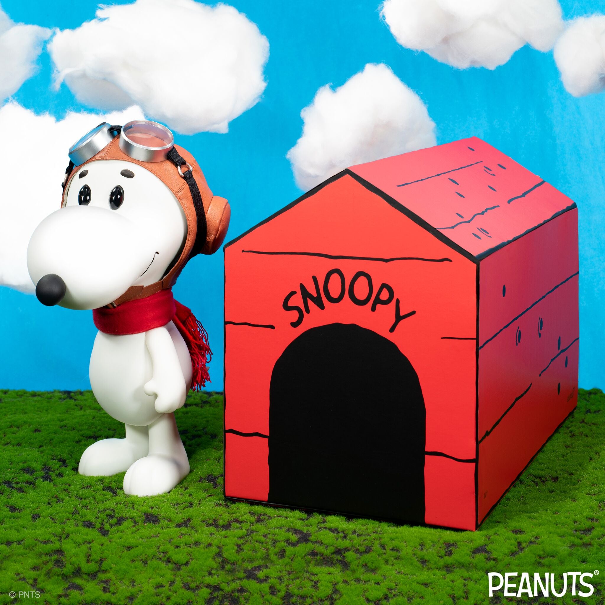 Snoopy from the Peanuts Flying Ace figure wearing aviator helmet and goggles beside a red doghouse against a bright blue sky.