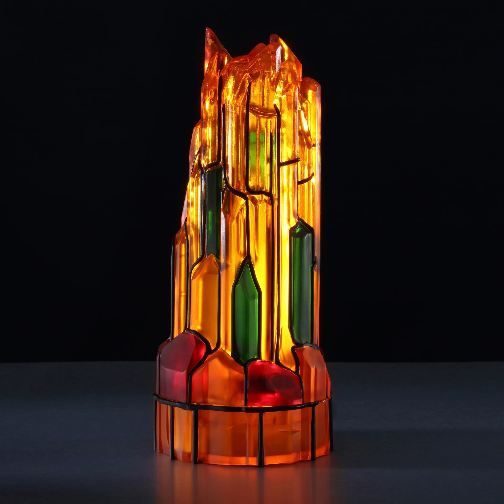 Abstract sculpture of orange, green, and red glass pieces with black outlines, glowing from within