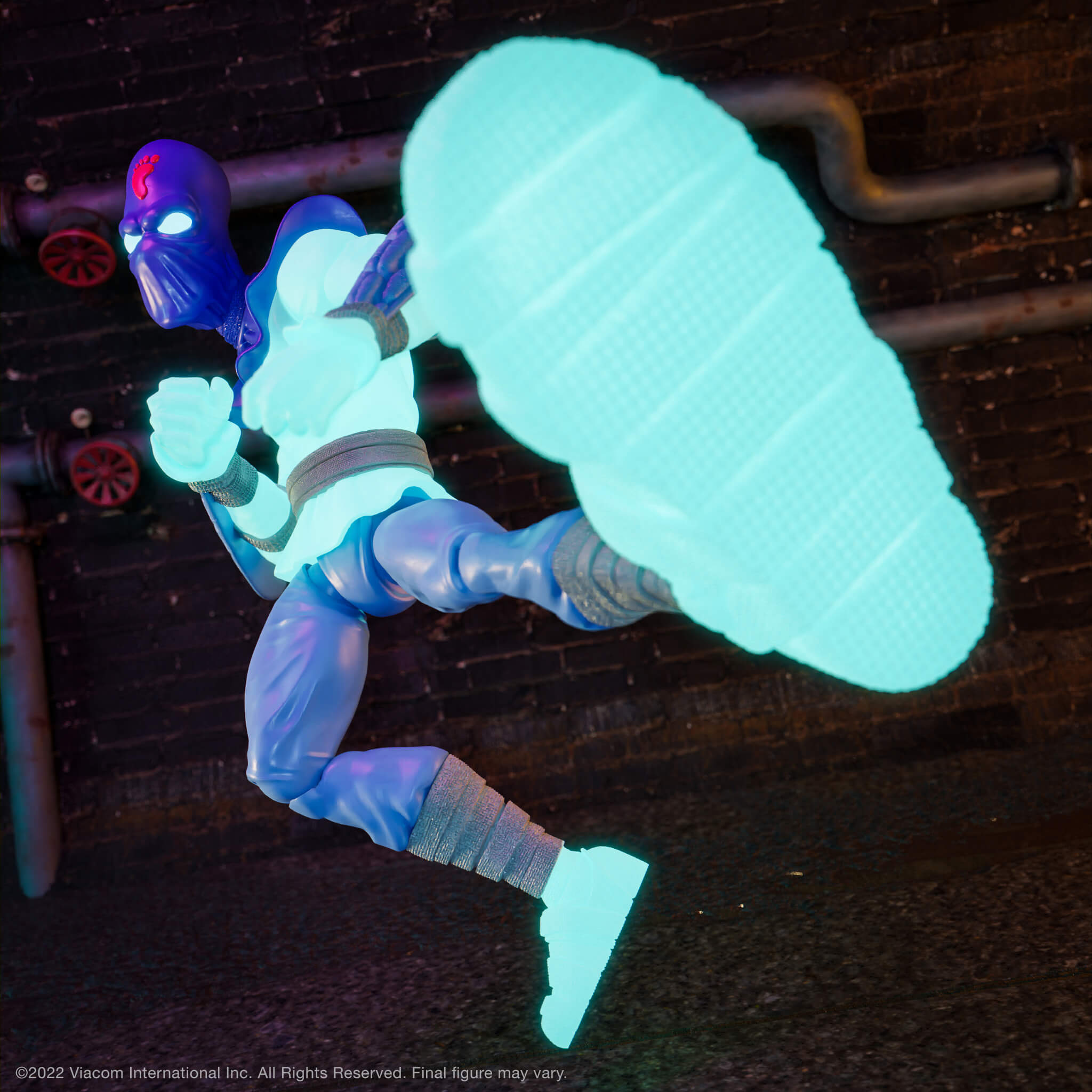 TMNT Ultimates Foot Soldier glow figure in a dynamic pose with a glowing cyan blade against a dark brick wall.