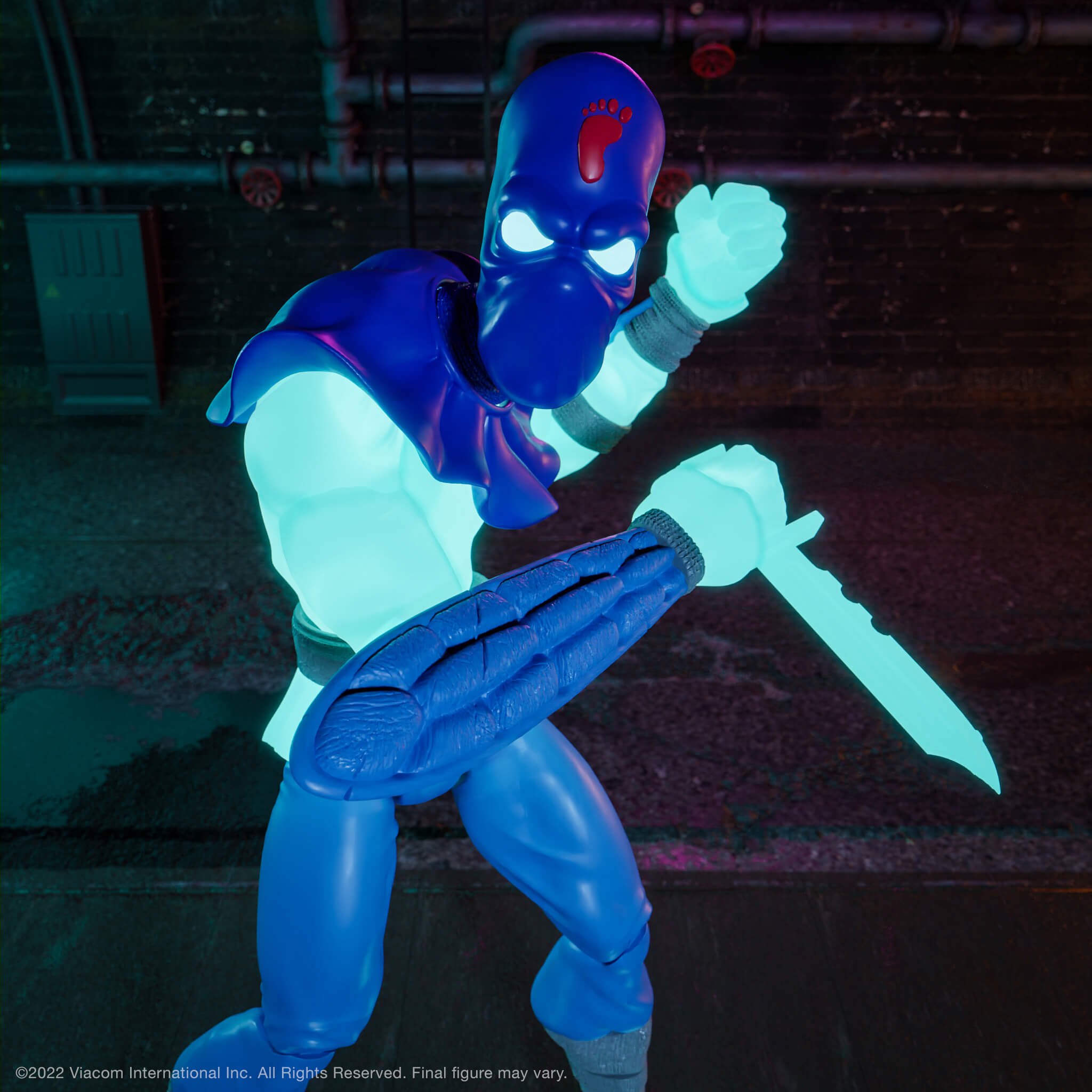 Foot Soldier glow figure posed in action with neon weapons against a dark industrial backdrop.
