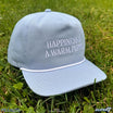 Light blue Happiness Hat with embroidered slogan on the crown resting on grass.